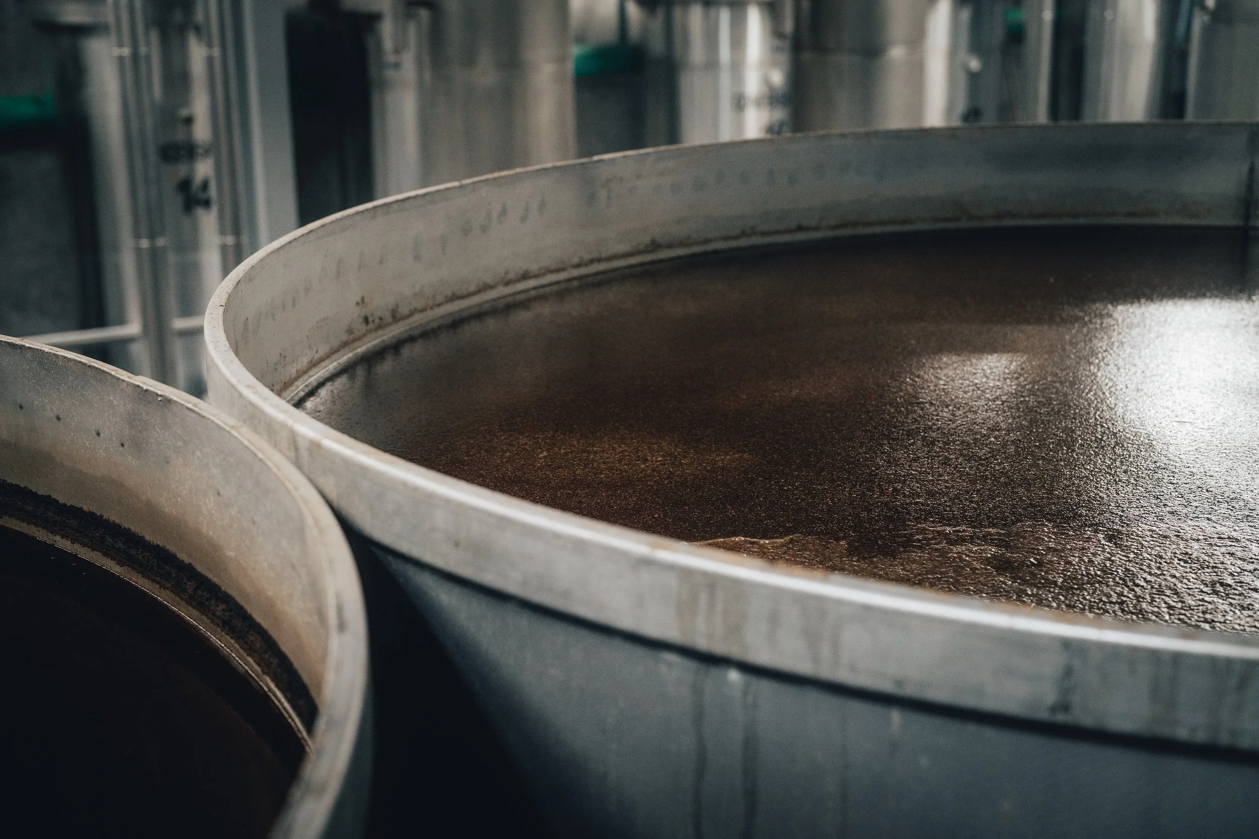 Close-up view of large metal tanks filled with dark liquid in an industrial setting.