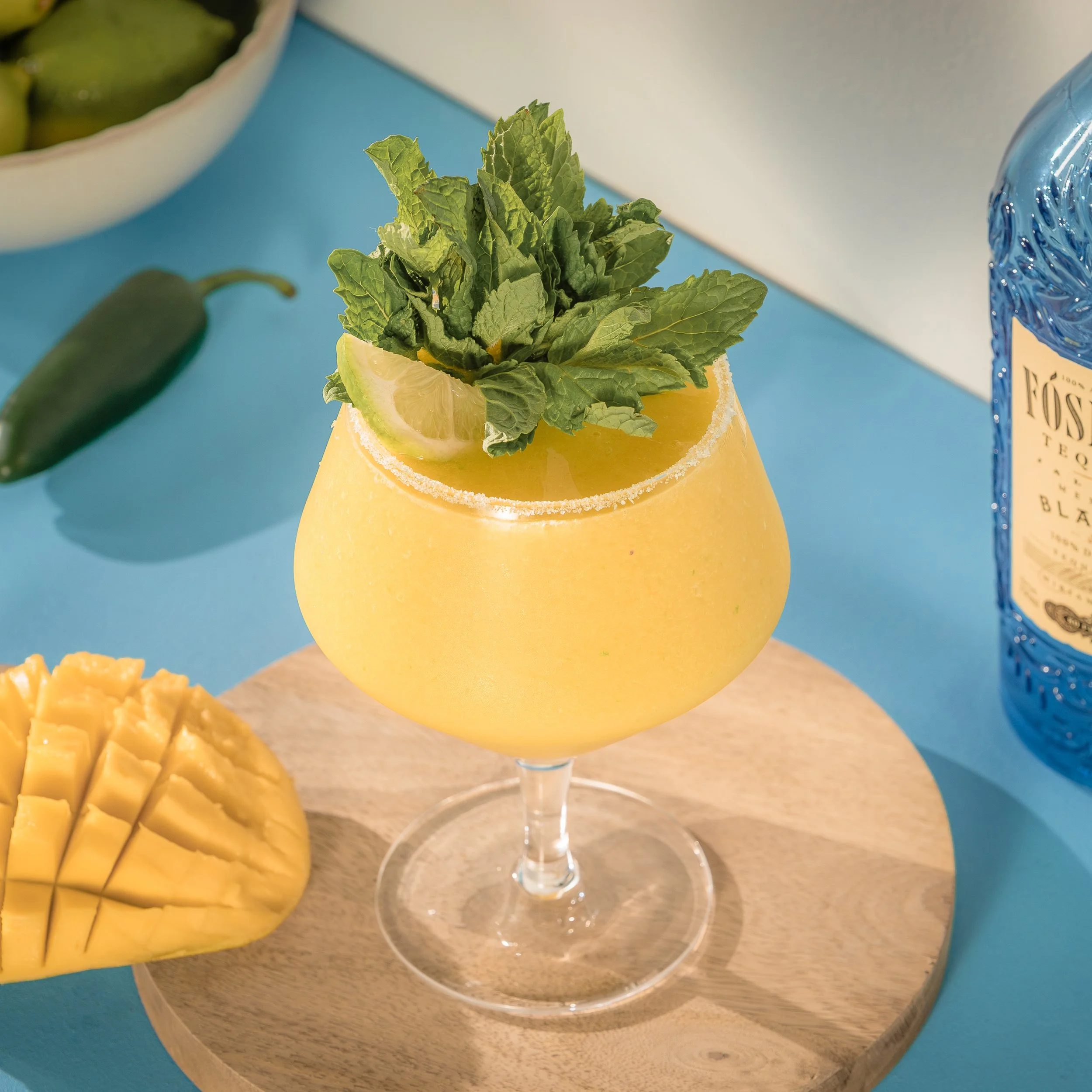 Frozen mango margarita with tequila, lime, and chili heat with mint garnish