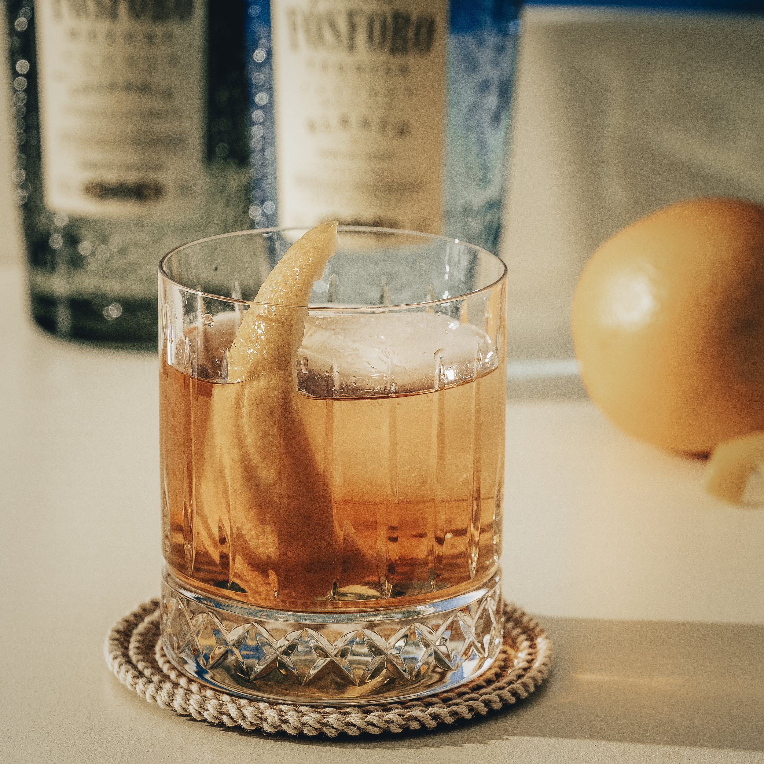 Old fashioned with mezcal, tequila, bitters, and citrus peel served over a large ice cube