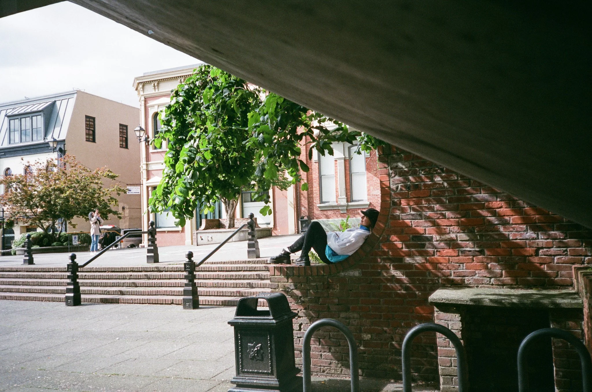 Person sitting in brick arch in urban setting with trees and buildings