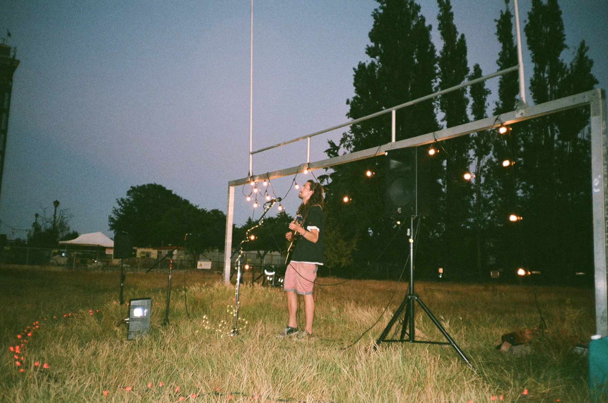 Outdoor music performance, evening, musician with guitar, string lights, grassy field