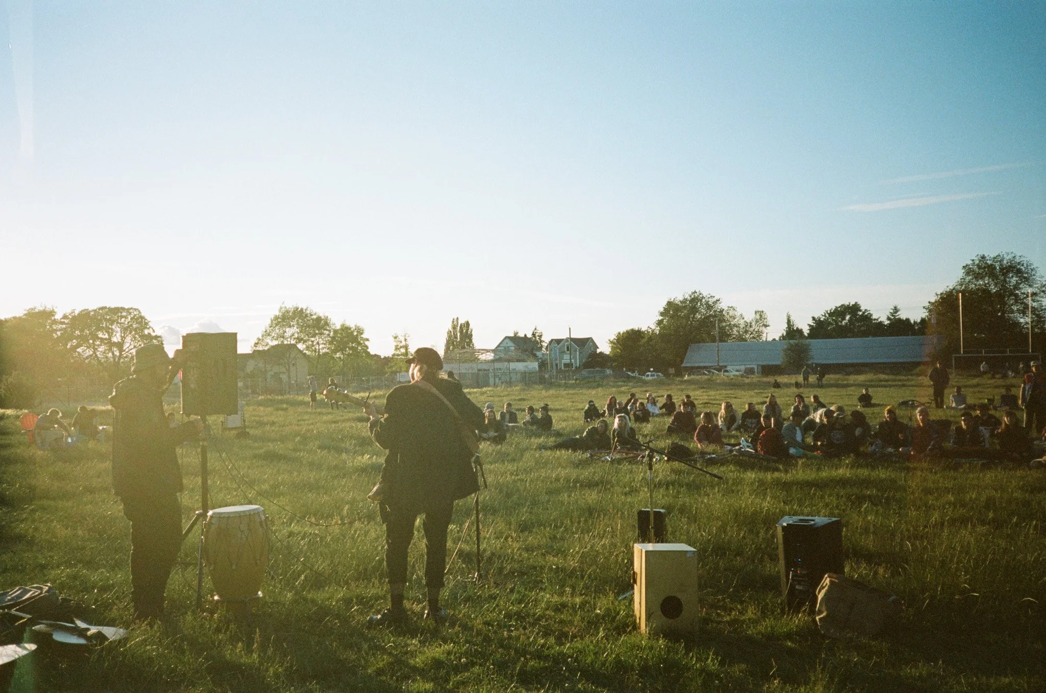 Outdoor concert in a field with musicians and seated audience at sunset.