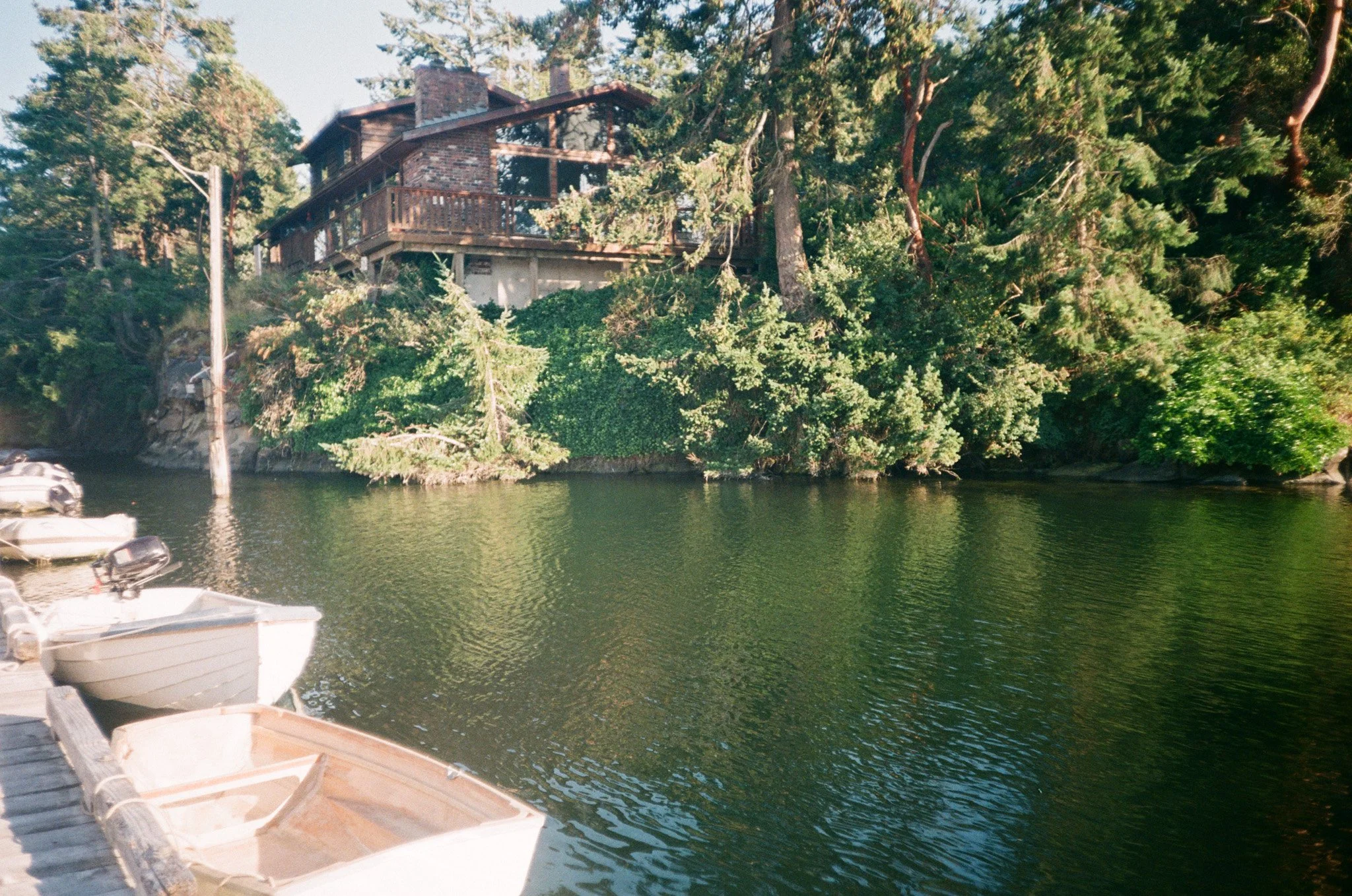 Lakeside house with wooden dock and small boats, surrounded by dense trees and greenery.