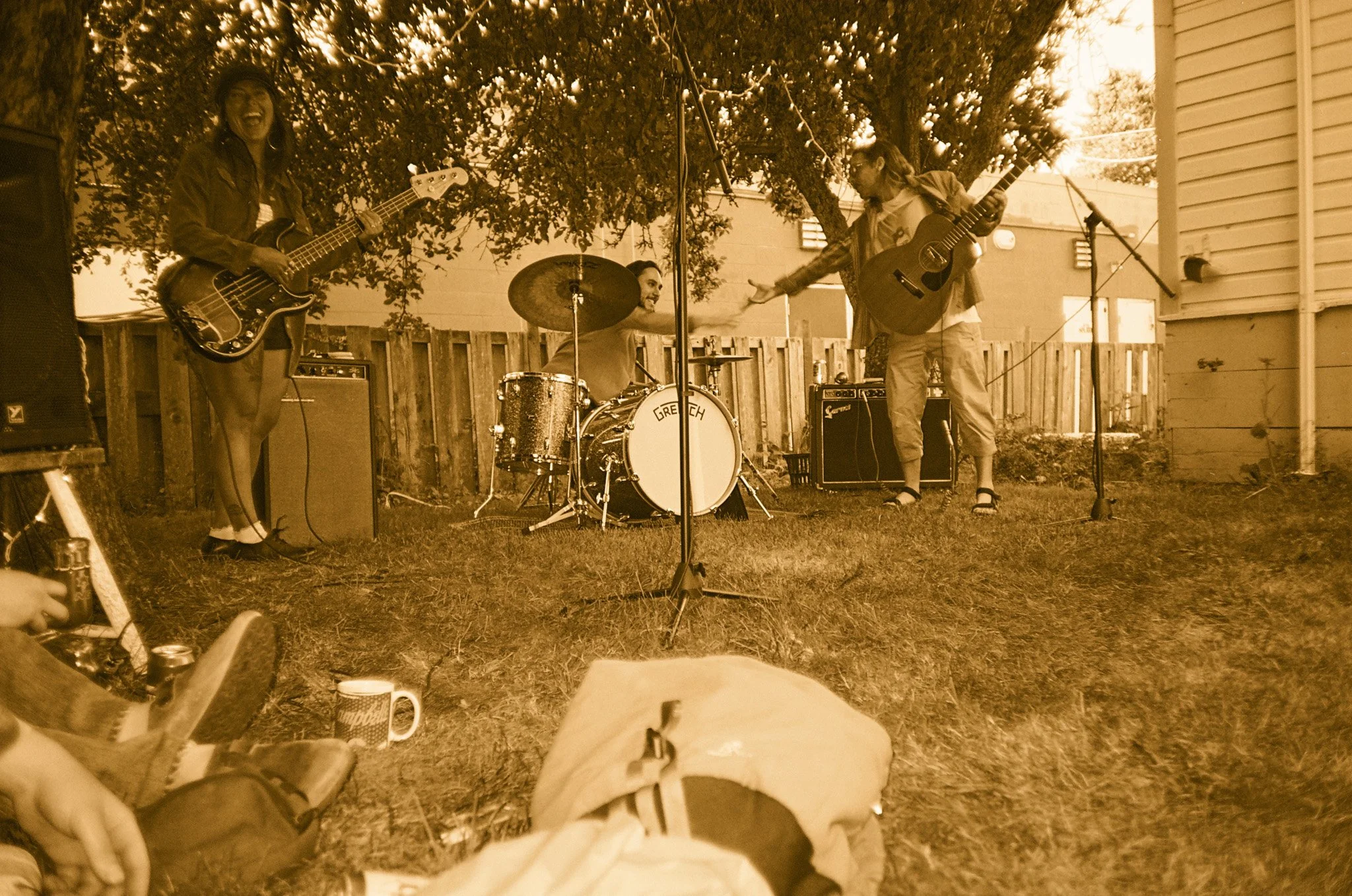 Sepia-tone outdoor jam session with musicians playing guitar and drums, surrounded by trees.