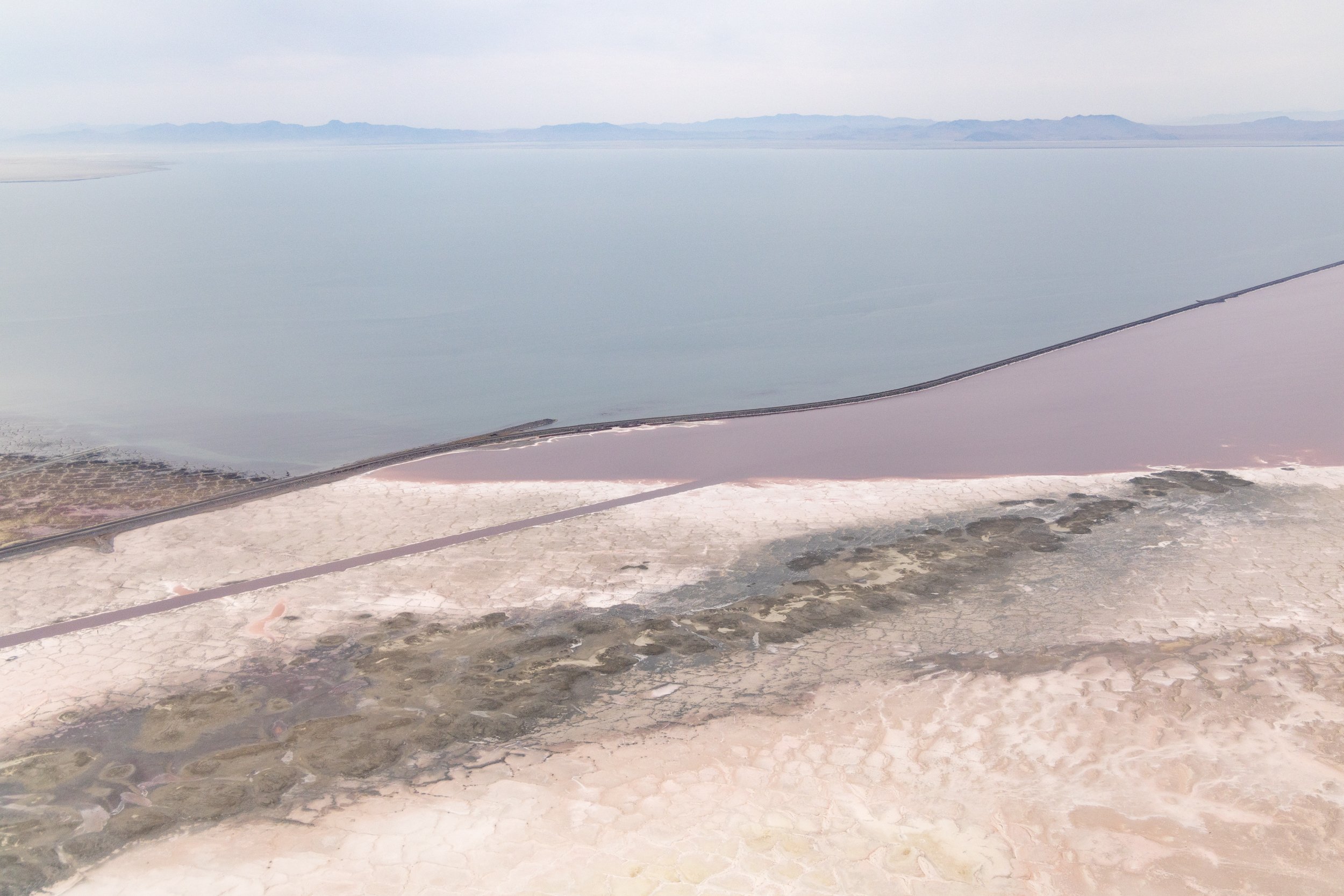  A railroad causeway divides the lake into two arms, north and south.  To the north, the water is pink and devoid of bird-sustaining invertebrates due to its extreme high salt concentration.  The south arm is still blue or green, but is in danger of 