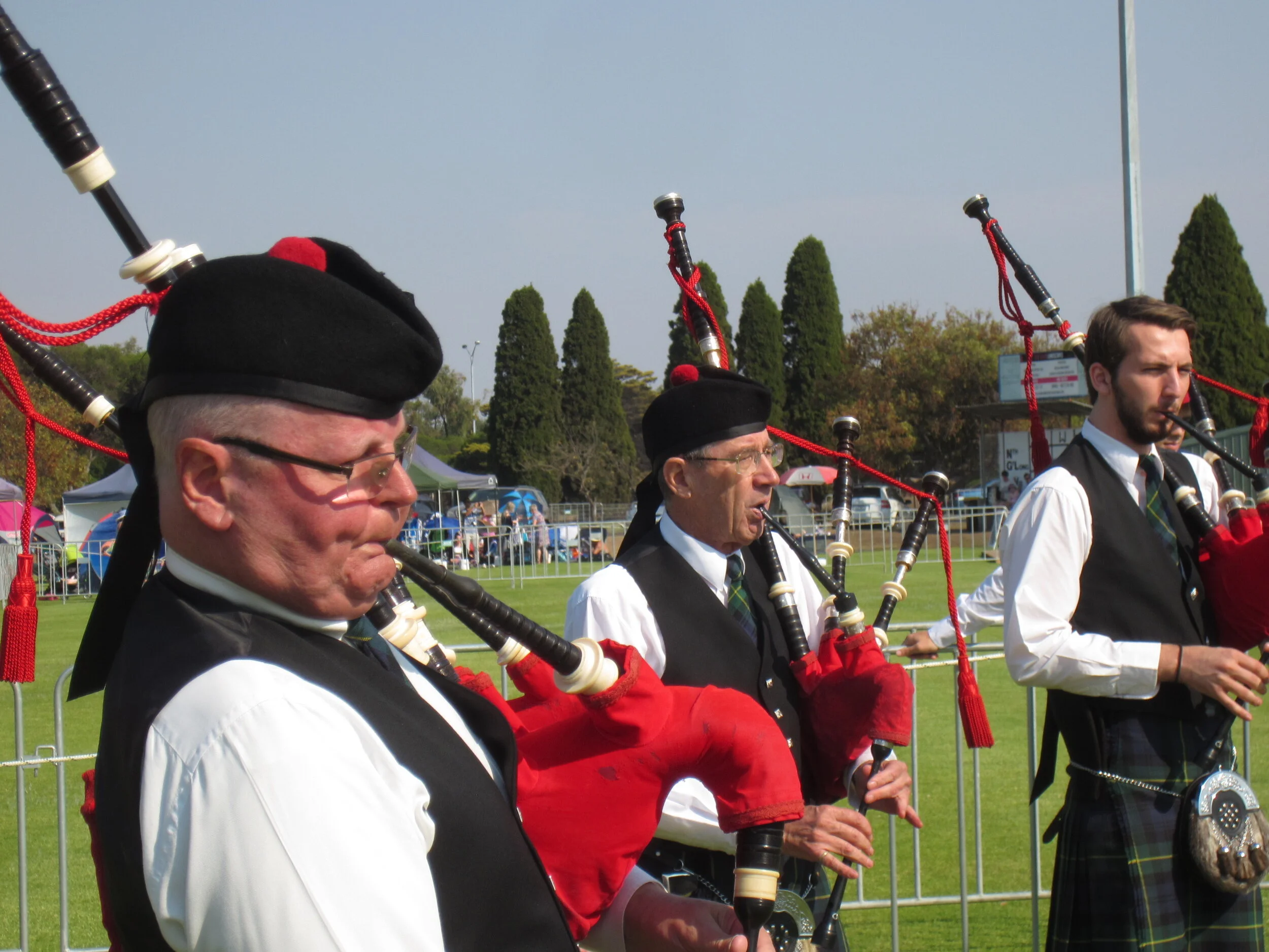 Men dressed in traditional Scottish attire playing bagpipes outdoors on a grassy field
