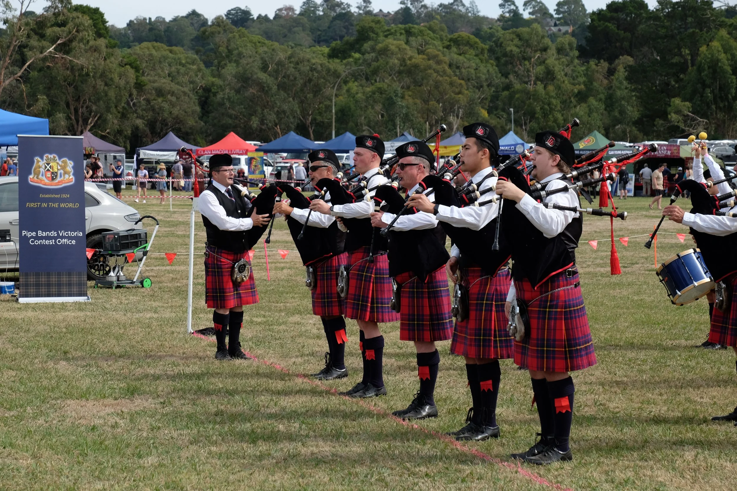 A group of musicians dressed in traditional Scottish attire, including tartan kilts, playing bagpipes during an outdoor event.