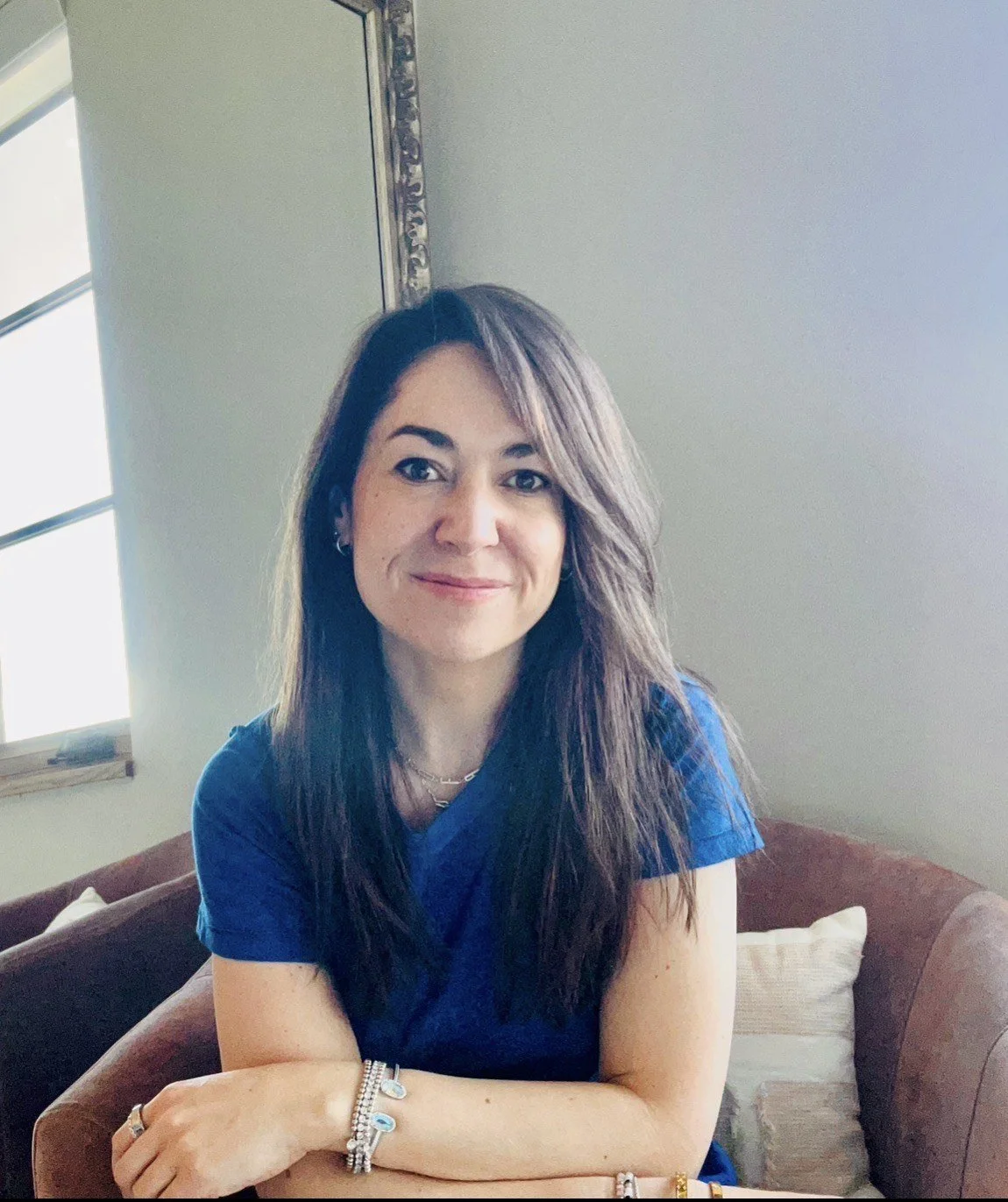 Woman therapist with a blue shirt sits on a brown chair with a friendly smile