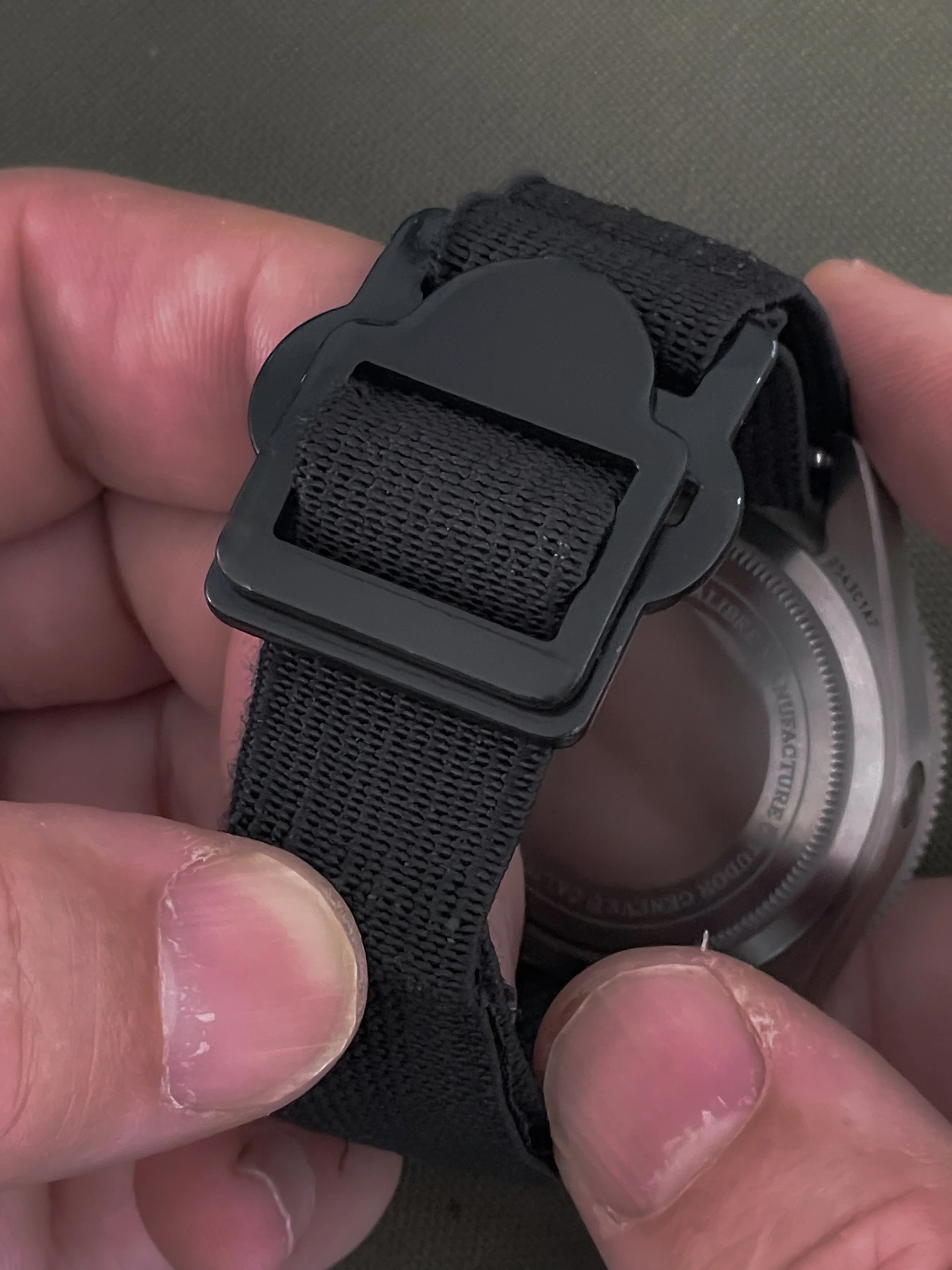 Close-up of a person's hands adjusting a black watch strap with a rectangular buckle on a silver watch case.