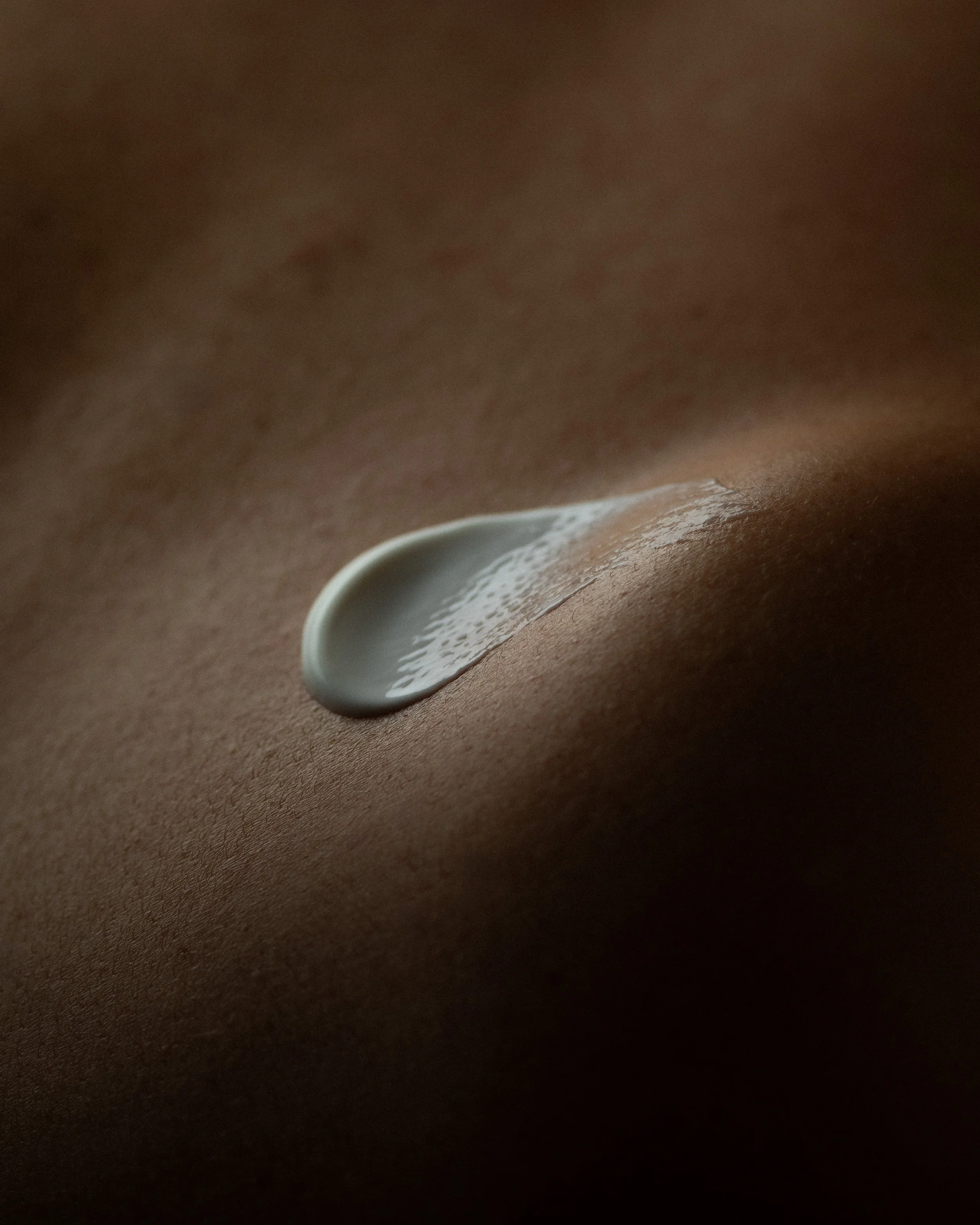 Close-up of a single drop of white lotion or cream on smooth human skin.