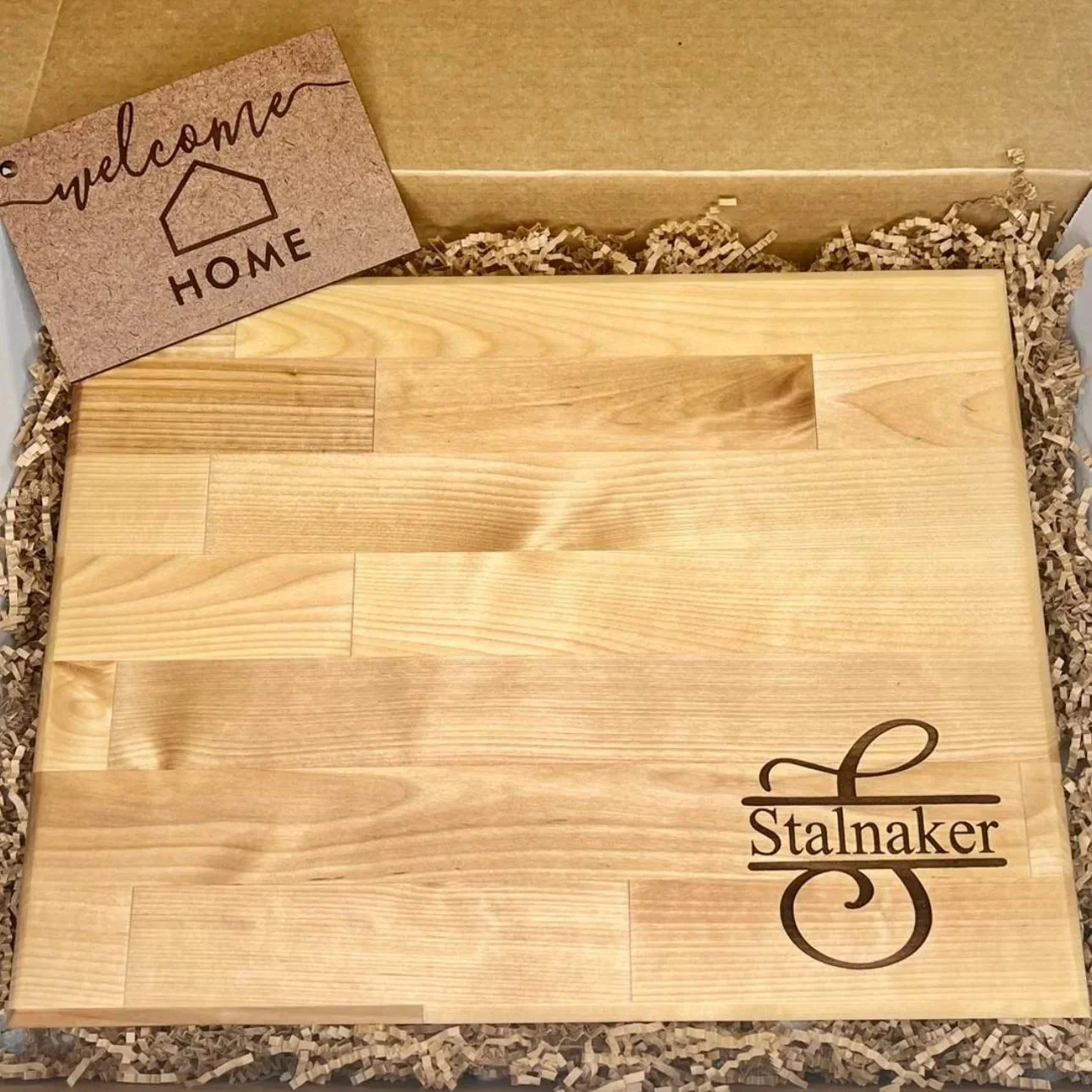 Personalized wooden welcome sign reading “Stalnaker,” packaged in a gift box with shredded paper filler and a welcome home tag