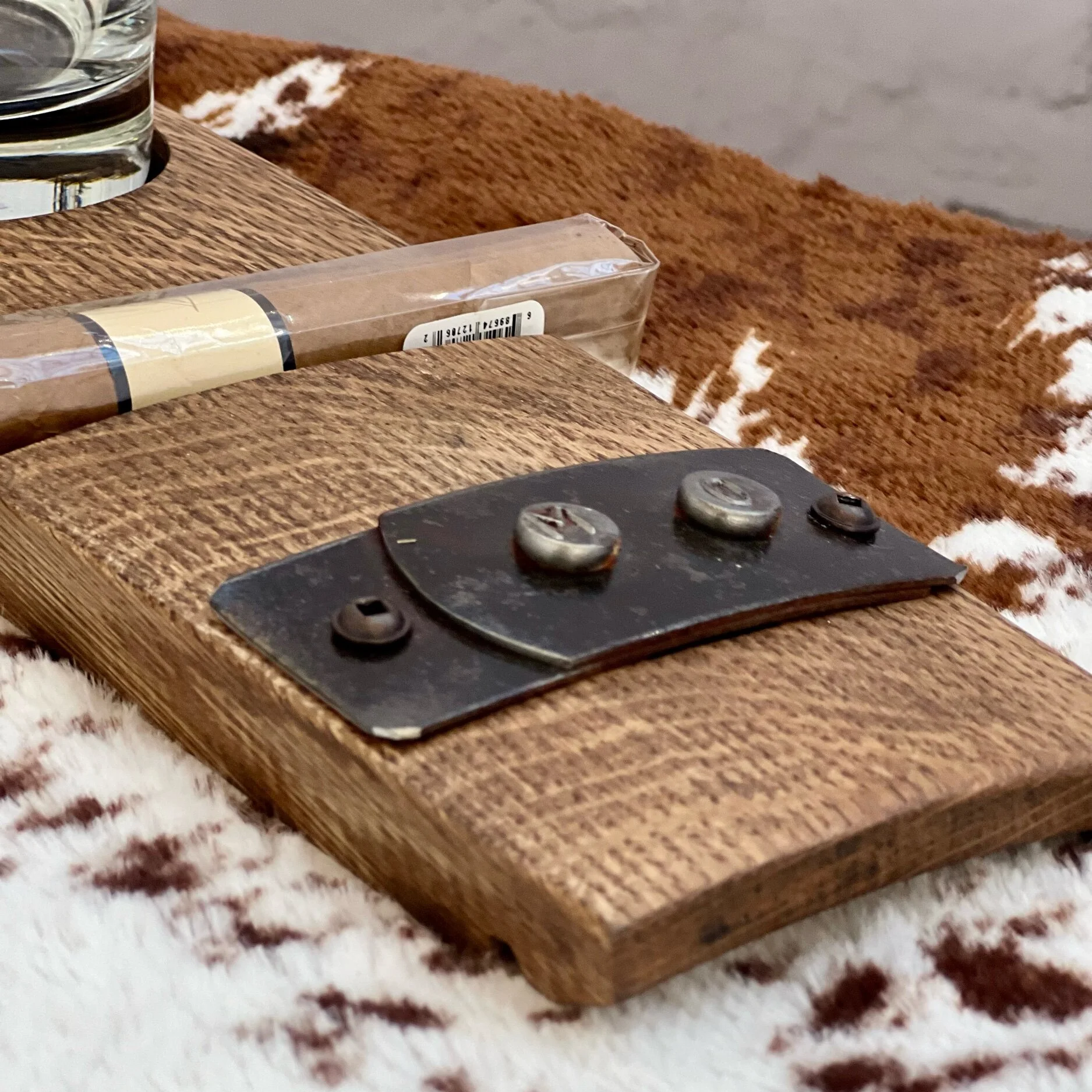 Wooden coffee table with a black metal hinge plate, a packaged tool, and a glass of water on a patterned rug