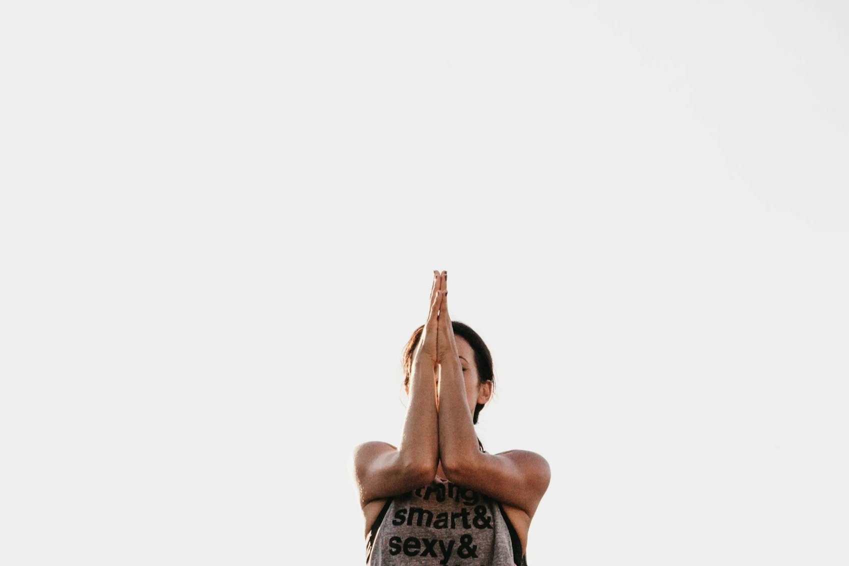 A woman practicing yoga outdoors with her hands in prayer position, facing towards the sky.