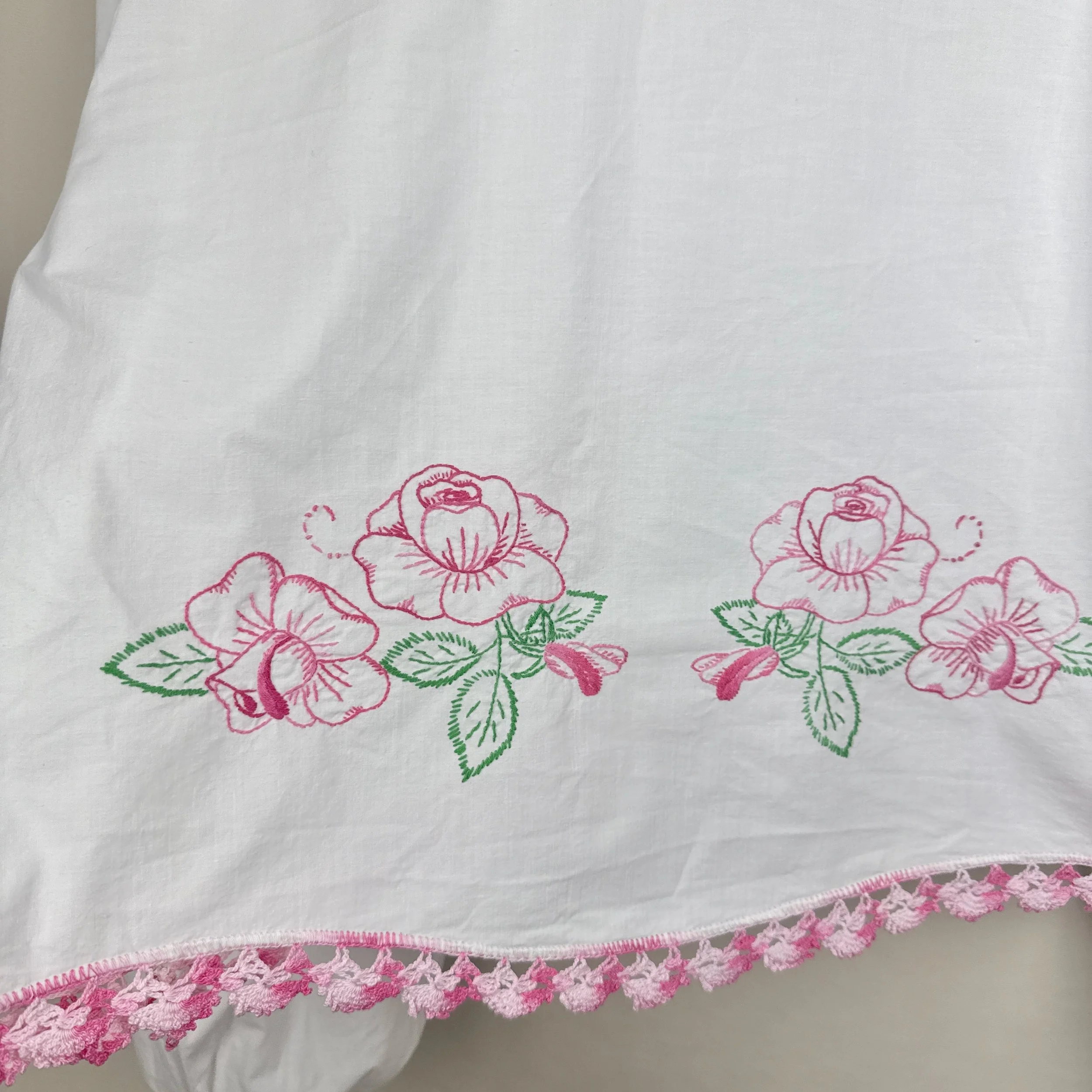 “White embroidered blouse upcycled from vintage bedsheet with pink floral details and crochet trim.