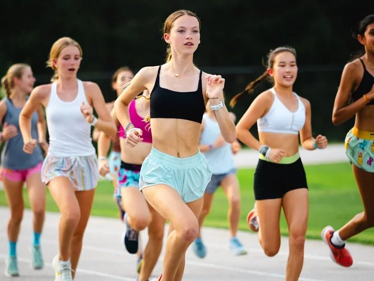 Youth girls running on track during outdoor race.
