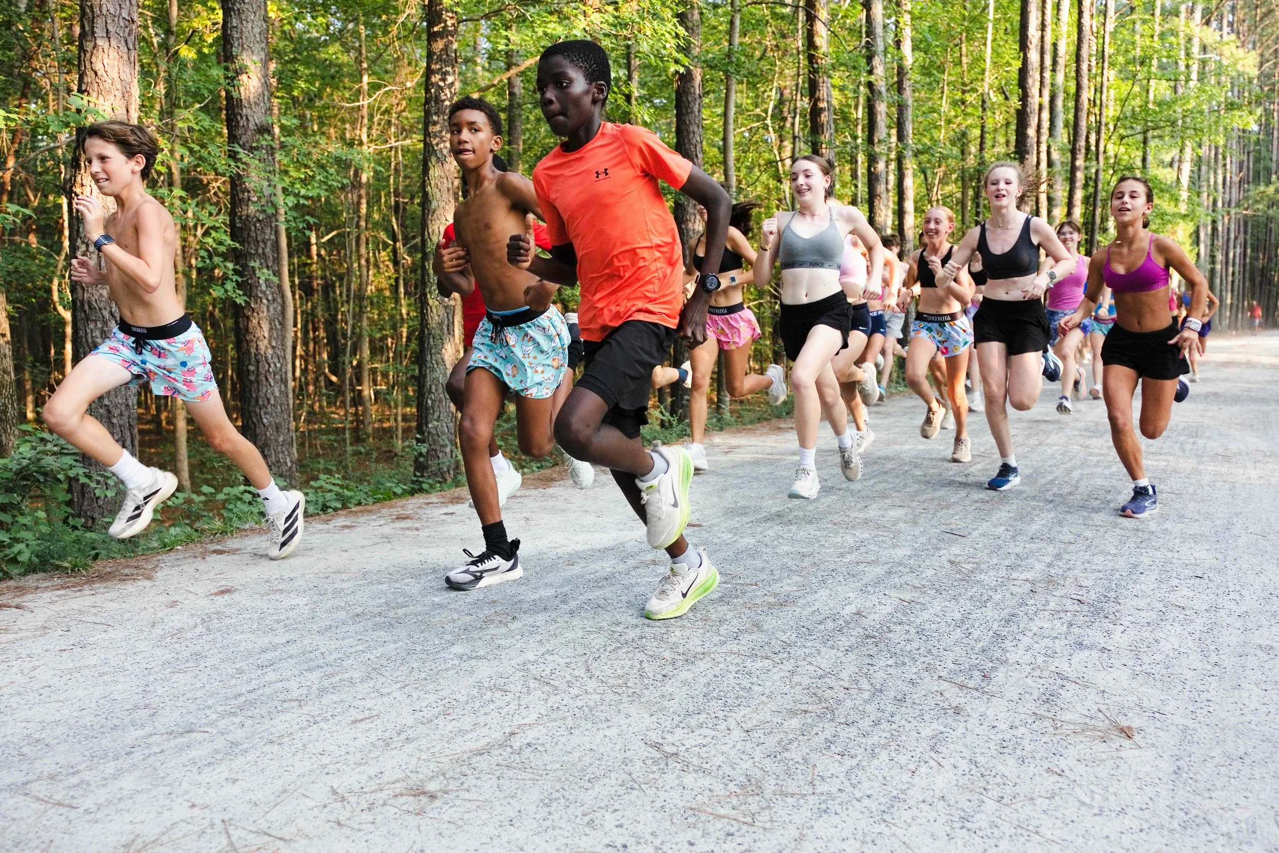 Group of children and teenagers running on a forest trail during daytime.