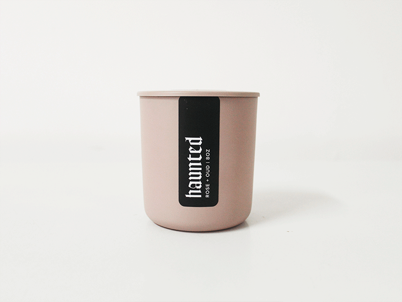 A pink candle with a black label reading "haunted" and scent "rosé + oud 8oz"