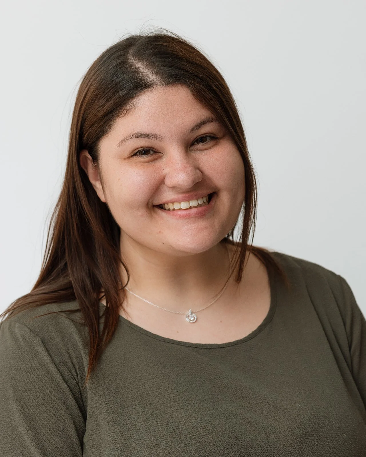 A young woman with shoulder-length brown hair smiling, wearing a green top and a silver necklace with a circular pendant.