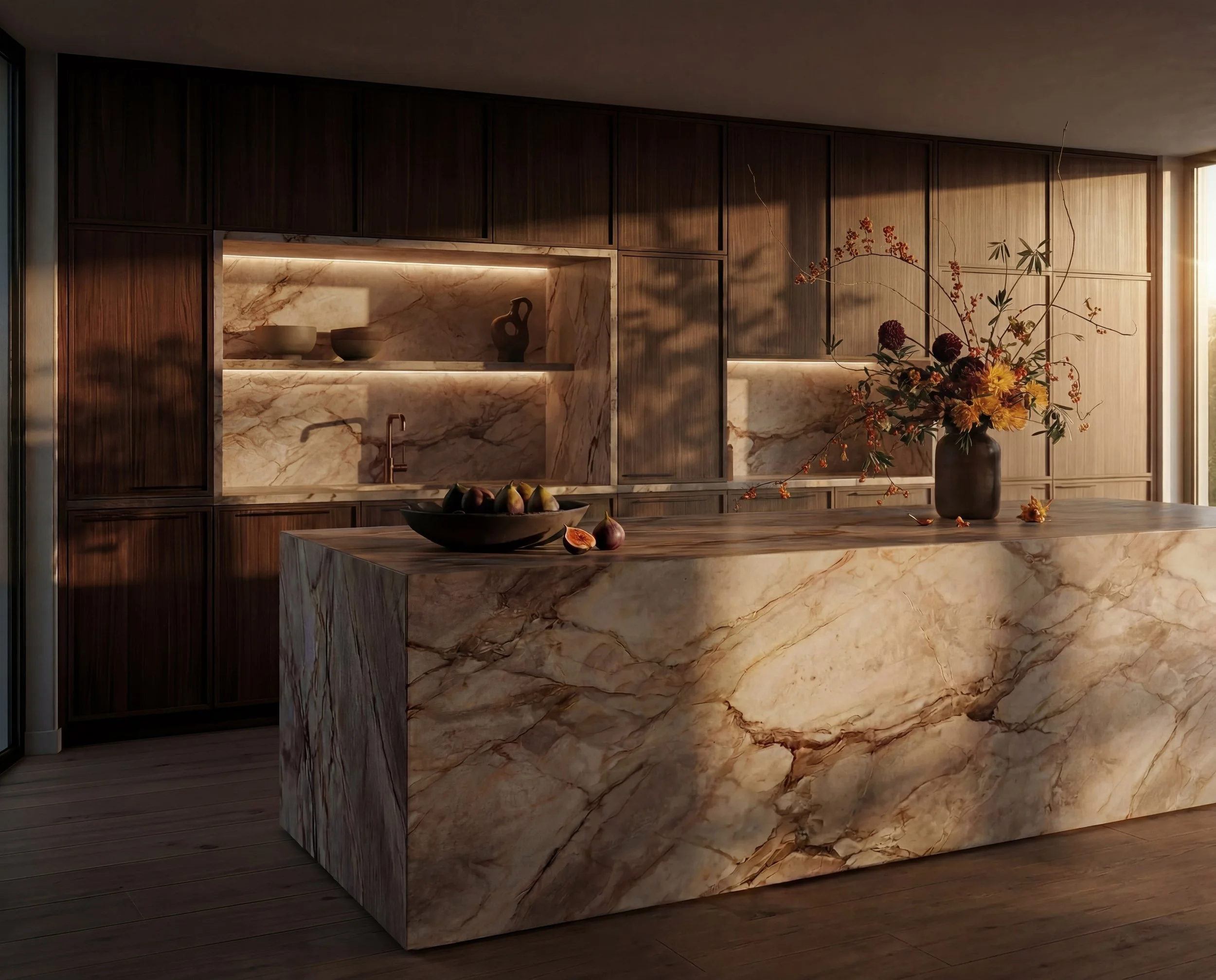A modern kitchen with a large marble island and matching marble backsplash, decorated with a flower arrangement in a dark vase and fruit in a bowl, with warm lighting creating a cozy ambiance.