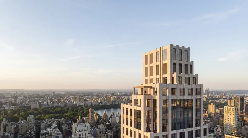 A tall, modern high-rise building in New York City with a cityscape and a river in the background during sunset.