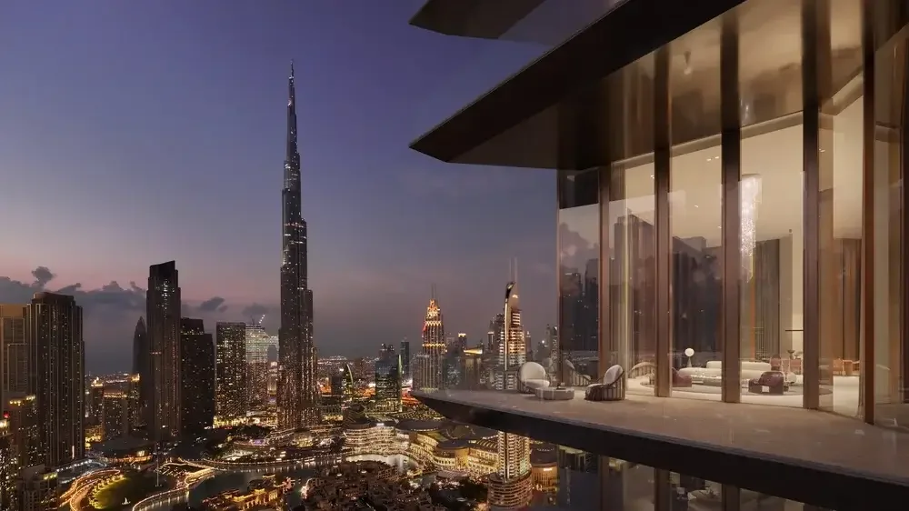 Nighttime city skyline view of Dubai with the Burj Khalifa, from a high-rise balcony with glass walls and modern outdoor seating.