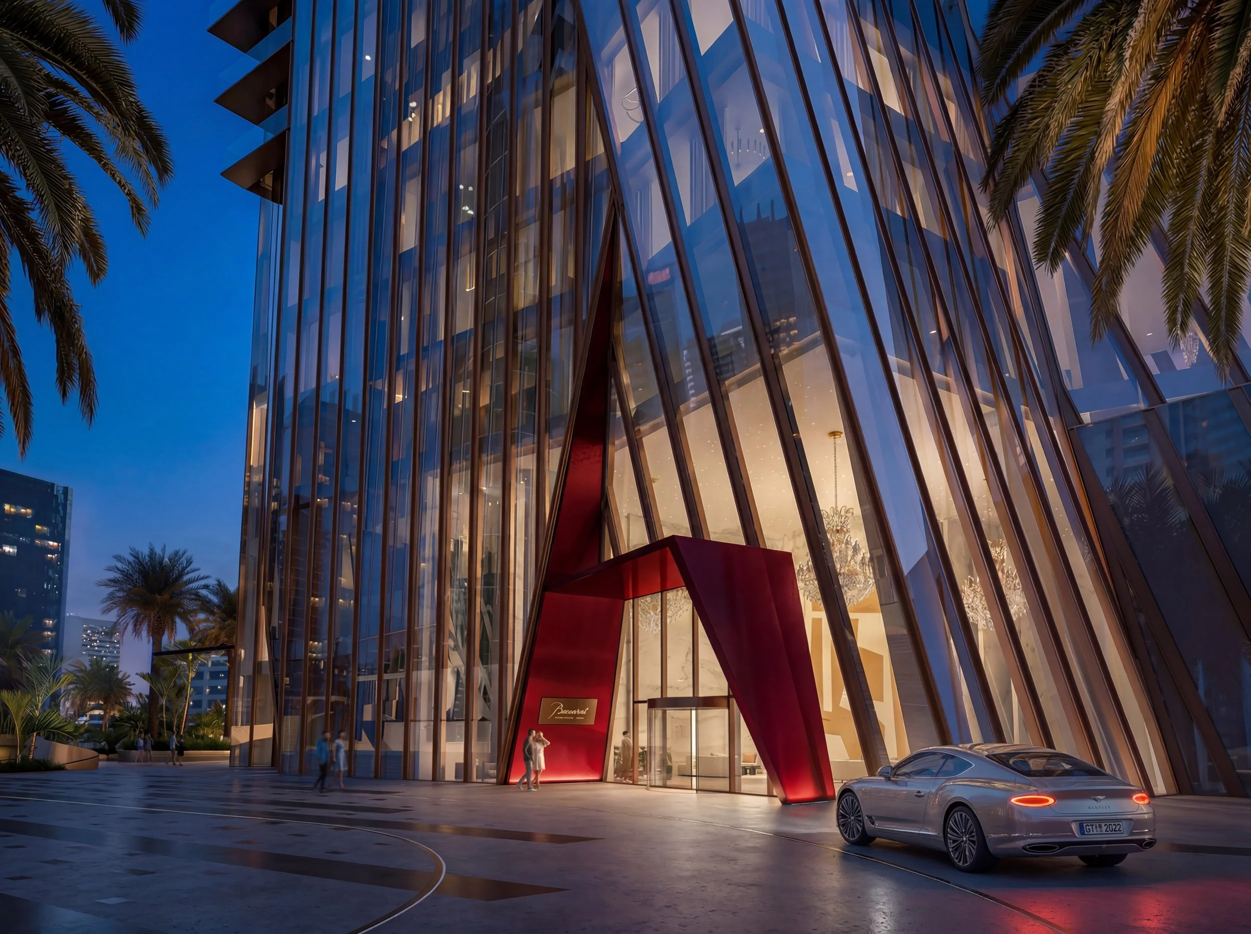 Nighttime view of a modern glass building with angled windows, palm trees in front, and a luxury car parked near the entrance