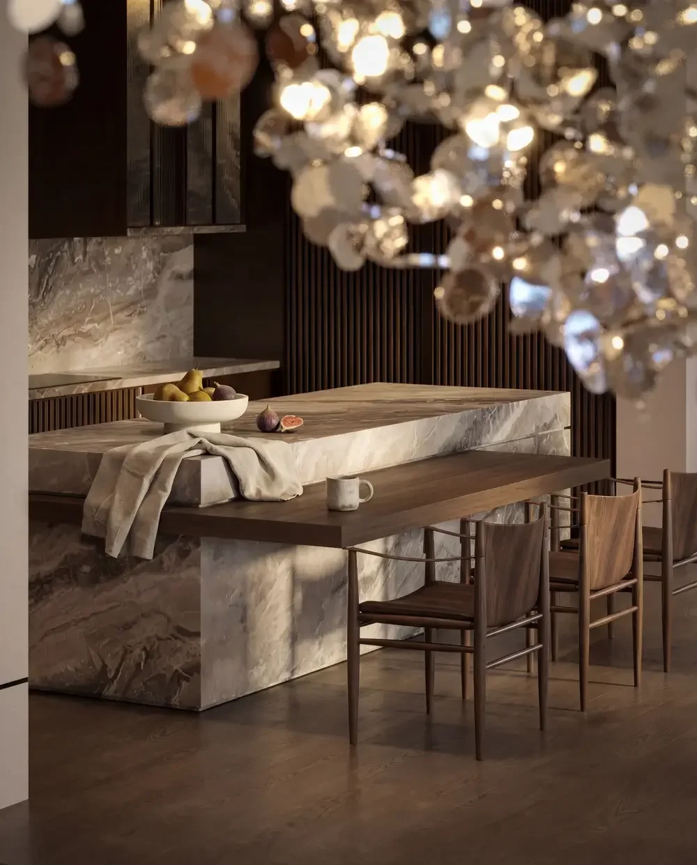 An elegant dining area featuring a large marble table with a beige and brown swirling pattern, accompanied by four wooden chairs with padded seats. A bowl of pears and figs rests on the table, alongside a mug and a cloth. The background includes a da