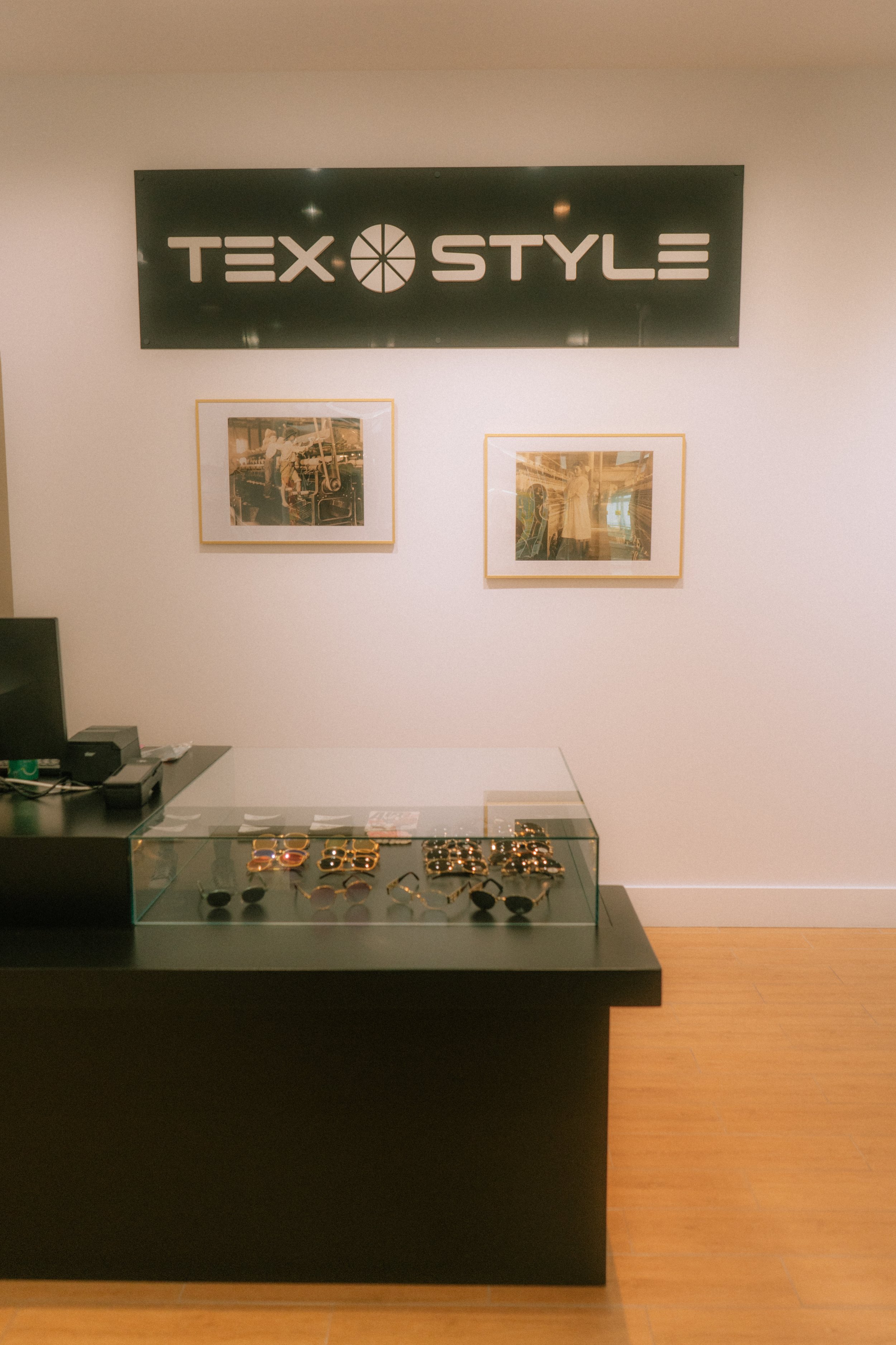 Store interior featuring sunglasses display case and TexStyle sign on wall with framed photographs.