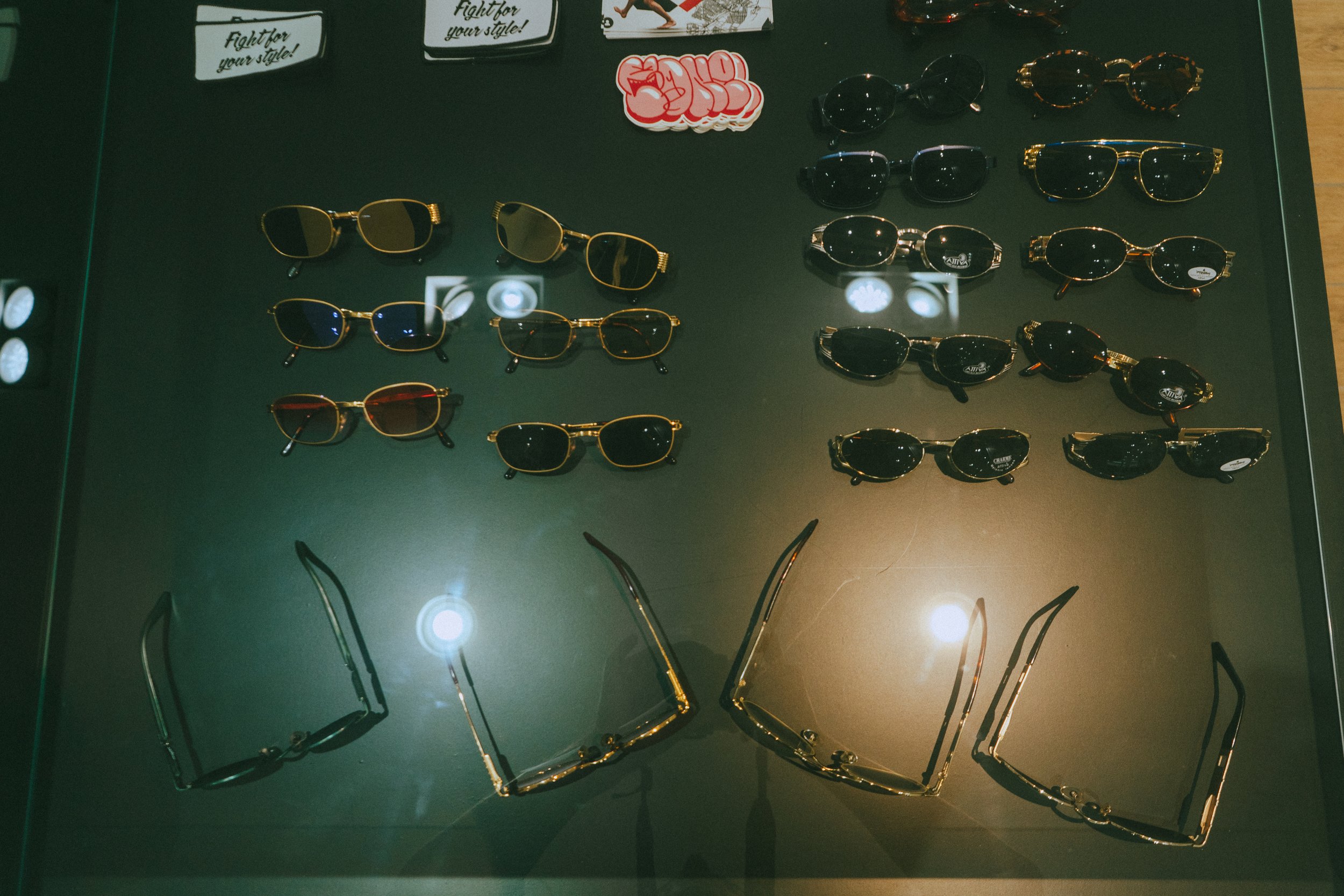 Display of various sunglasses on a showcase table with some accessories and stickers.