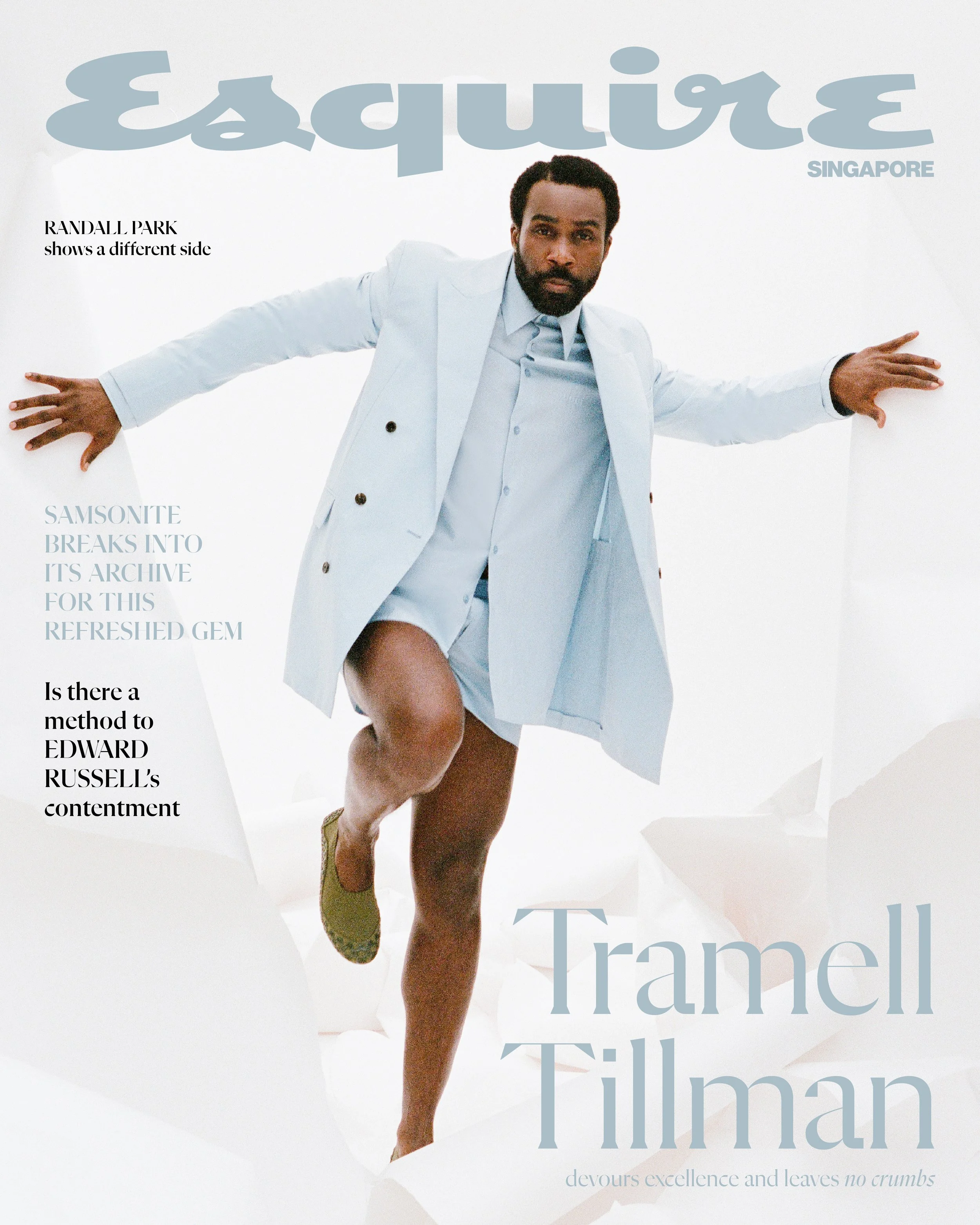 Magazine cover featuring a man in a light blue suit with one rolled-up pant leg, standing with arms extended and one leg raised, set against a white background with torn paper elements. The title 'Esquire' is in large blue letters at the top, with th