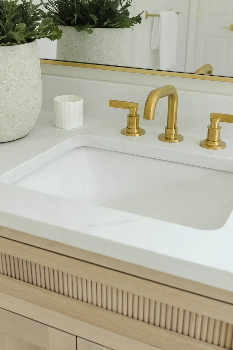 A close-up view of a luxury bathroom vanity, emphasizing the craftsmanship, materials, and refined details that define the space. The focal point is a sleek integrated sink carved into a crisp white countertop, creating a seamless and minimalist appe