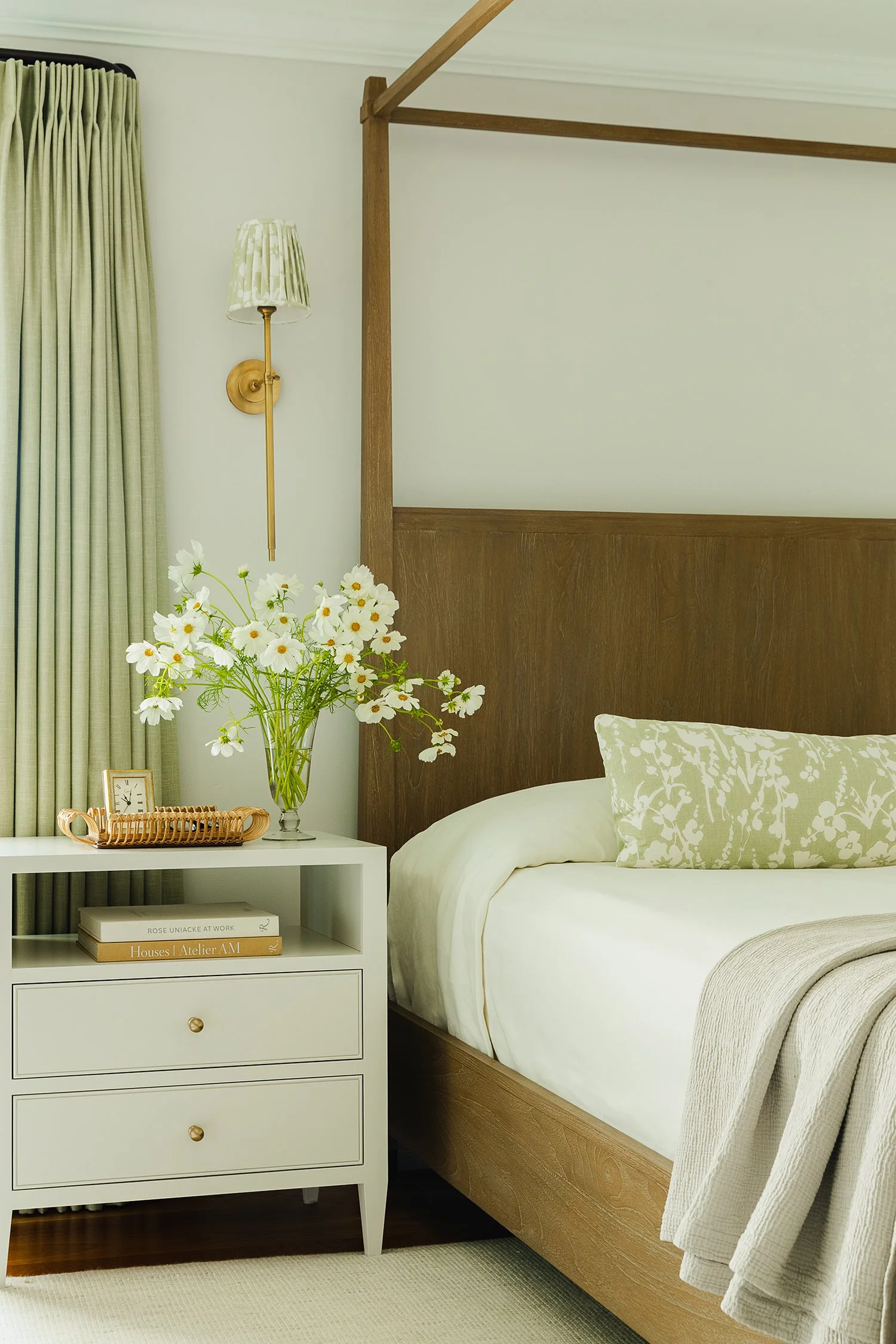 Luxury primary bedroom showcasing a custom walnut four-poster bed, layered neutral bedding, bespoke floral lumbar pillow, tailored bedside styling, and soft green drapery creating a timeless, sophisticated retreat.