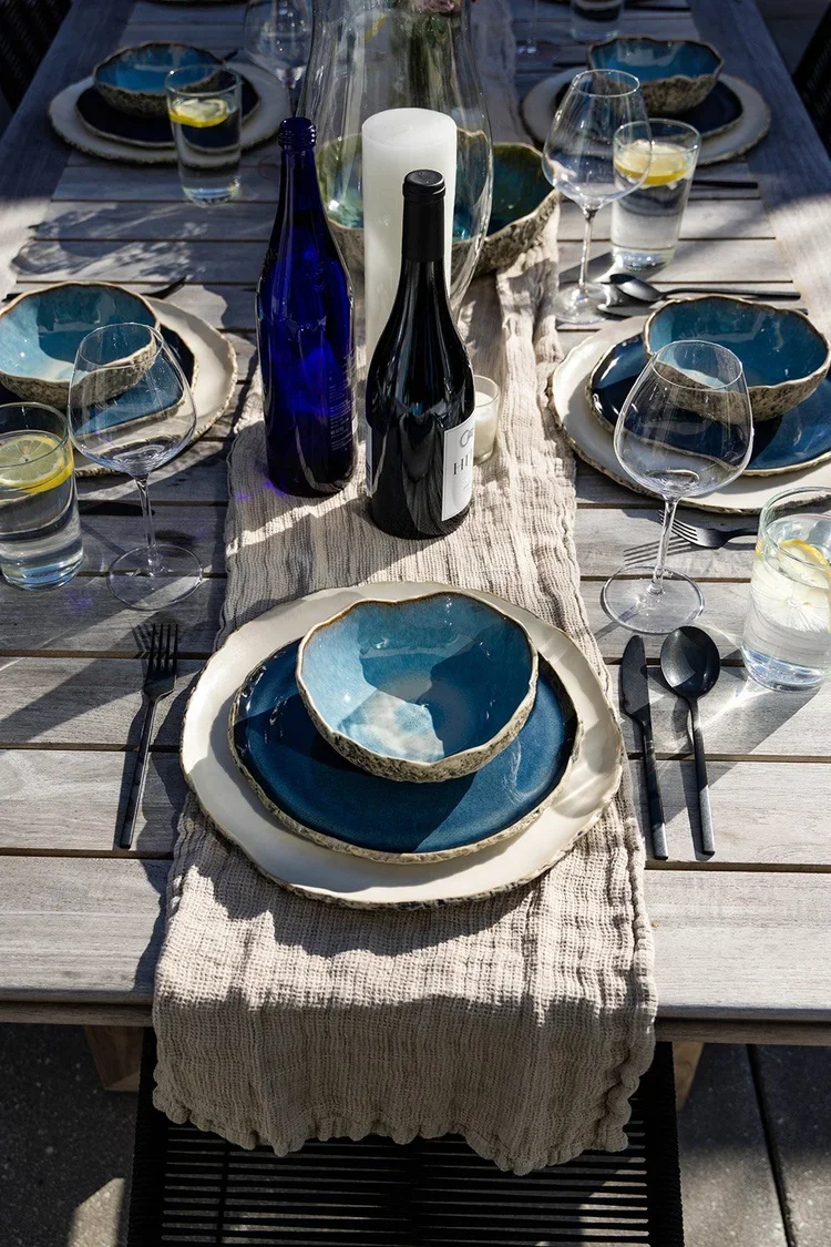 Hope Street | Rooftop Terrace Dining | Kate Kelly Interiors | Brooklyn, NY. Elegant outdoor tablescape featuring handcrafted blue ceramic dinnerware, textured linen runner, black flatware, crystal stemware, fresh florals, and a weathered wood dining 