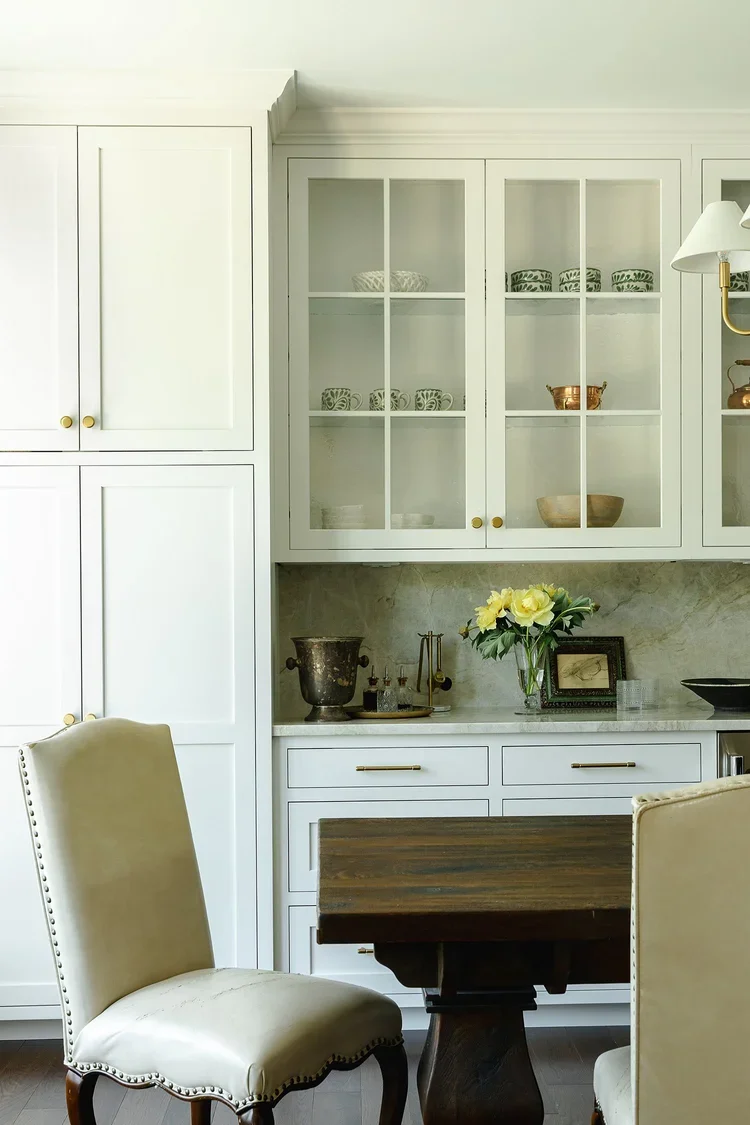 A beautifully integrated dining and entertaining area adjacent to a custom butler’s pantry. The space features floor-to-ceiling white cabinetry with a combination of solid-panel storage and glass-front display cabinets, creating a clean, tailored app