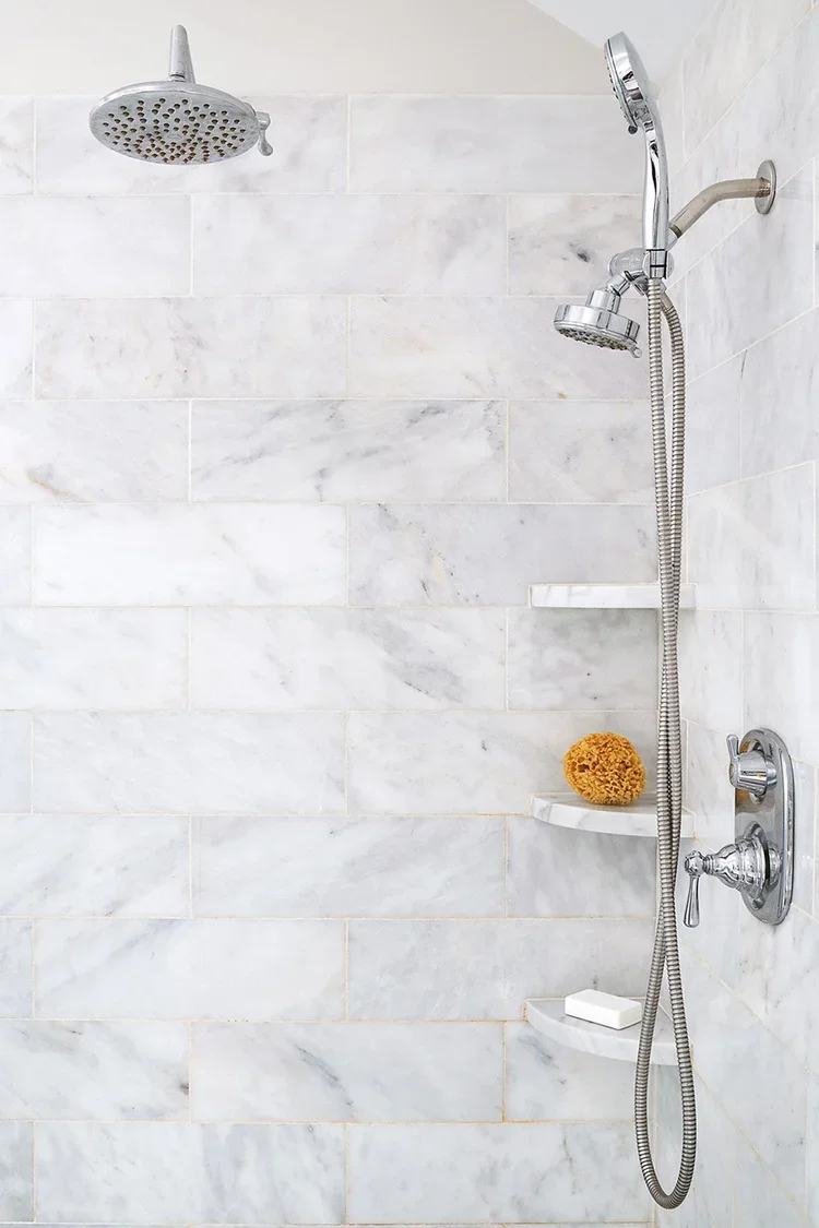 A close-up view of a luxurious walk-in shower clad in large-format white marble tiles with subtle gray veining. The clean, timeless tilework creates a bright and sophisticated backdrop, emphasizing the bathroom’s spa-like aesthetic.

Polished chrome 