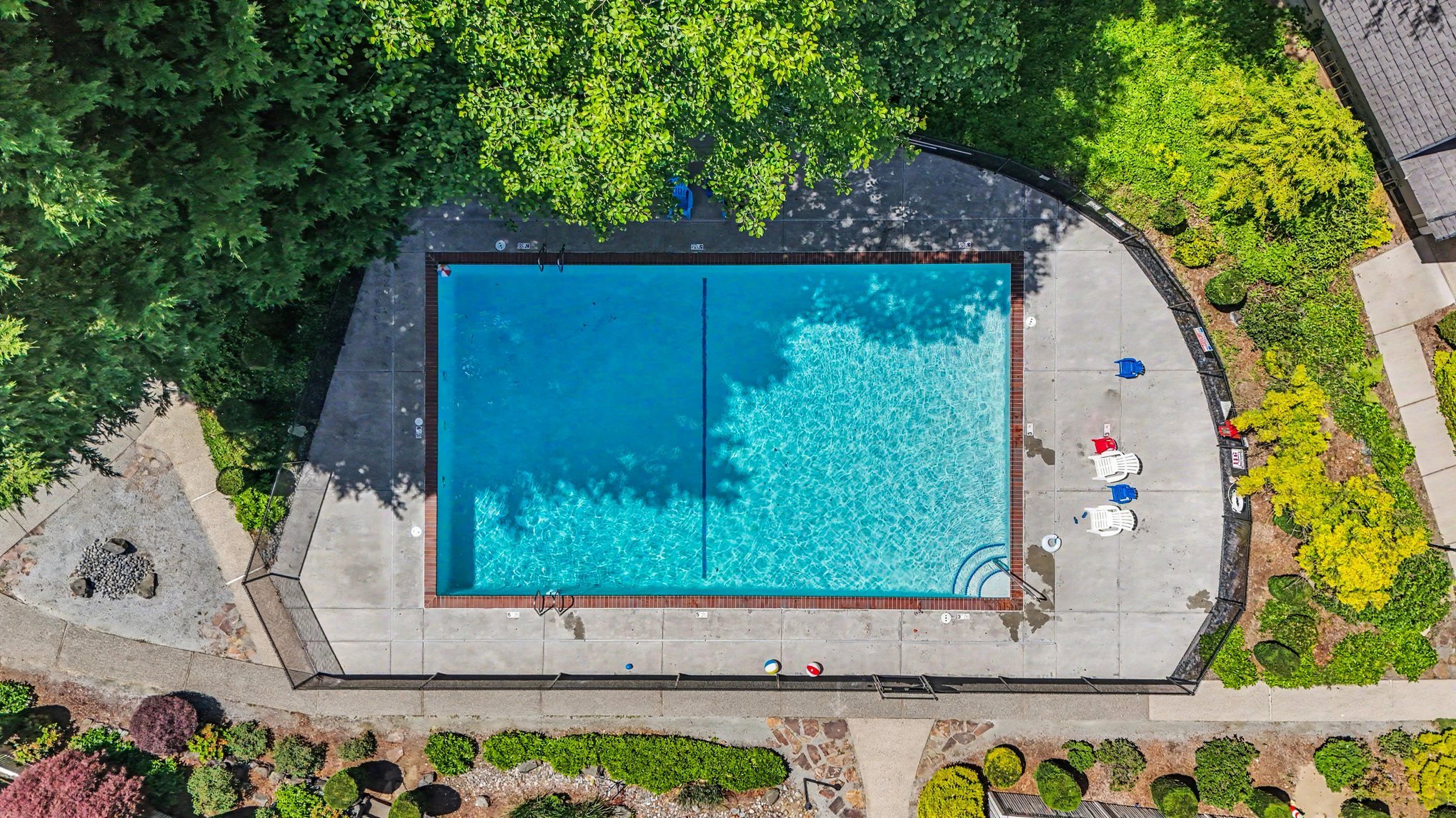 Aerial view of large sparkling pool, outdoor lounge area and greenbelt