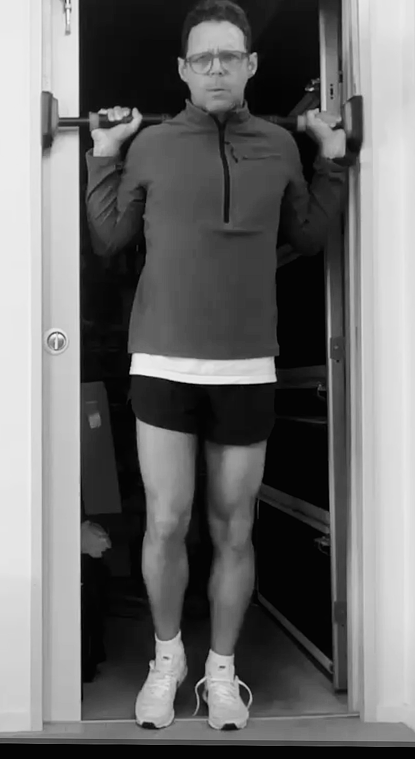 Physiotherapist Paul White performing a single-leg isometric calf raise using a doorway pull-up bar to create high load strength training for runners