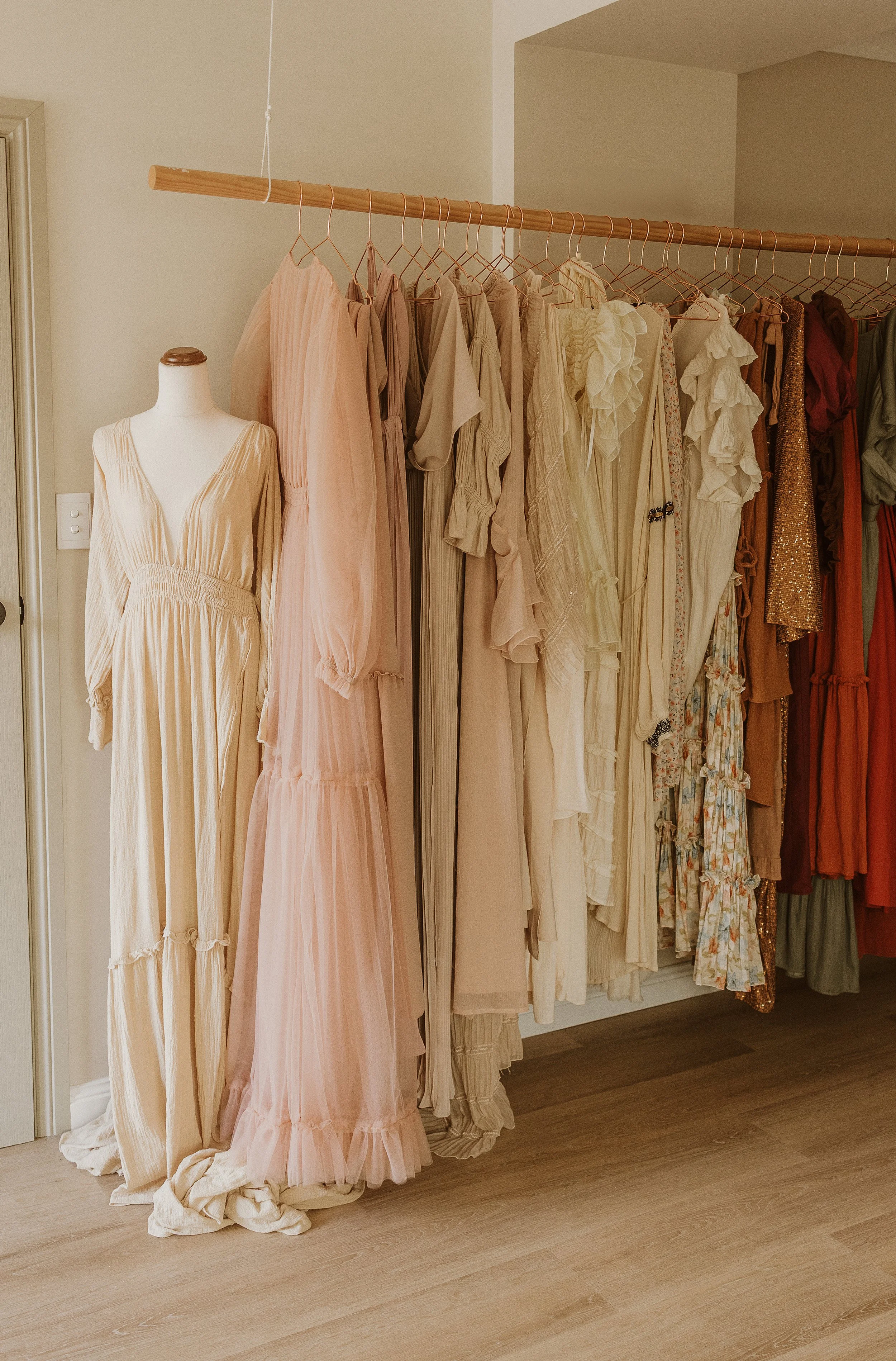 A display of pastel-colored and neutral dresses hanging on a clothing rack in a boutique or wardrobe.