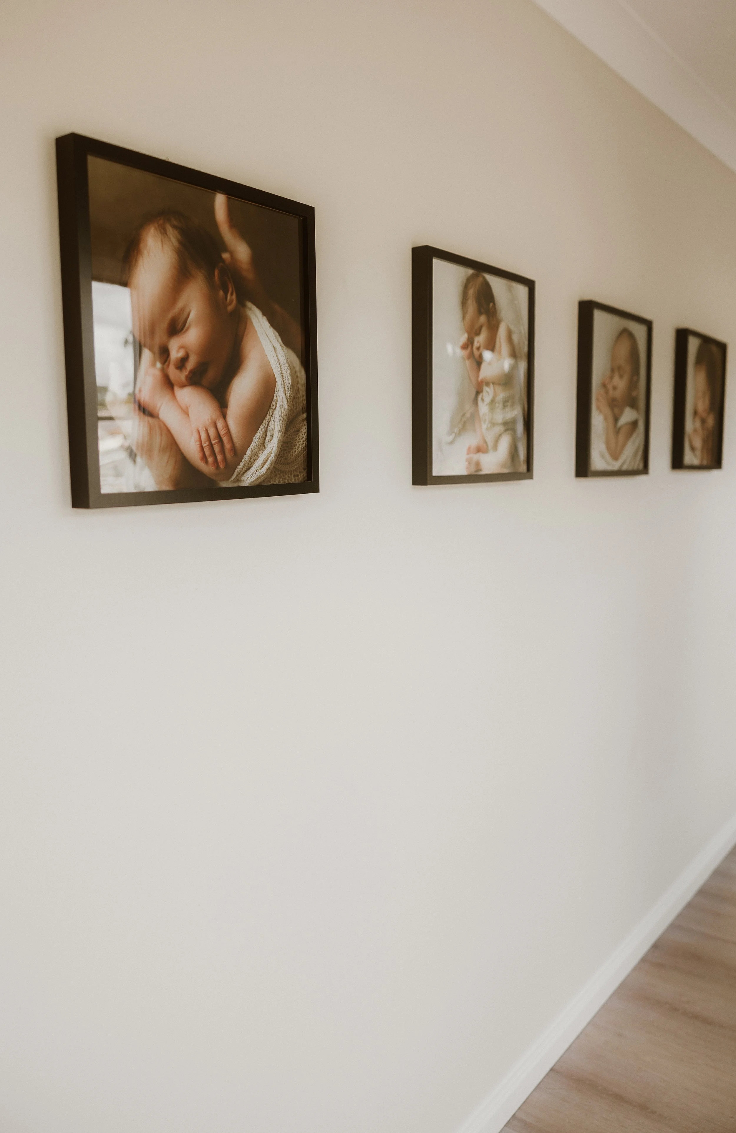 A wall hanging with four framed photographs of a baby girl sleeping and playing.