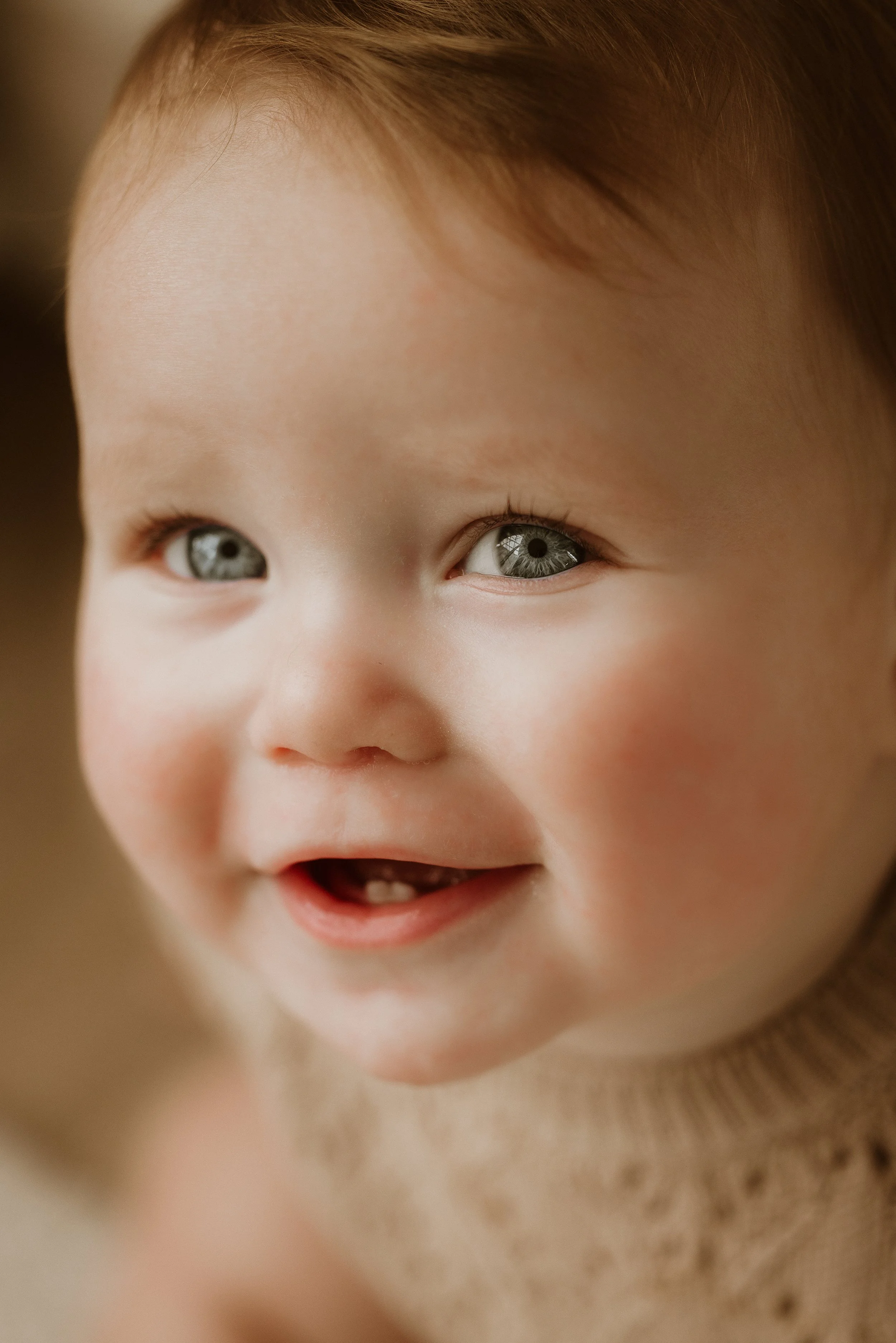 Close-up of a smiling toddler with blue eyes and light brown hair.