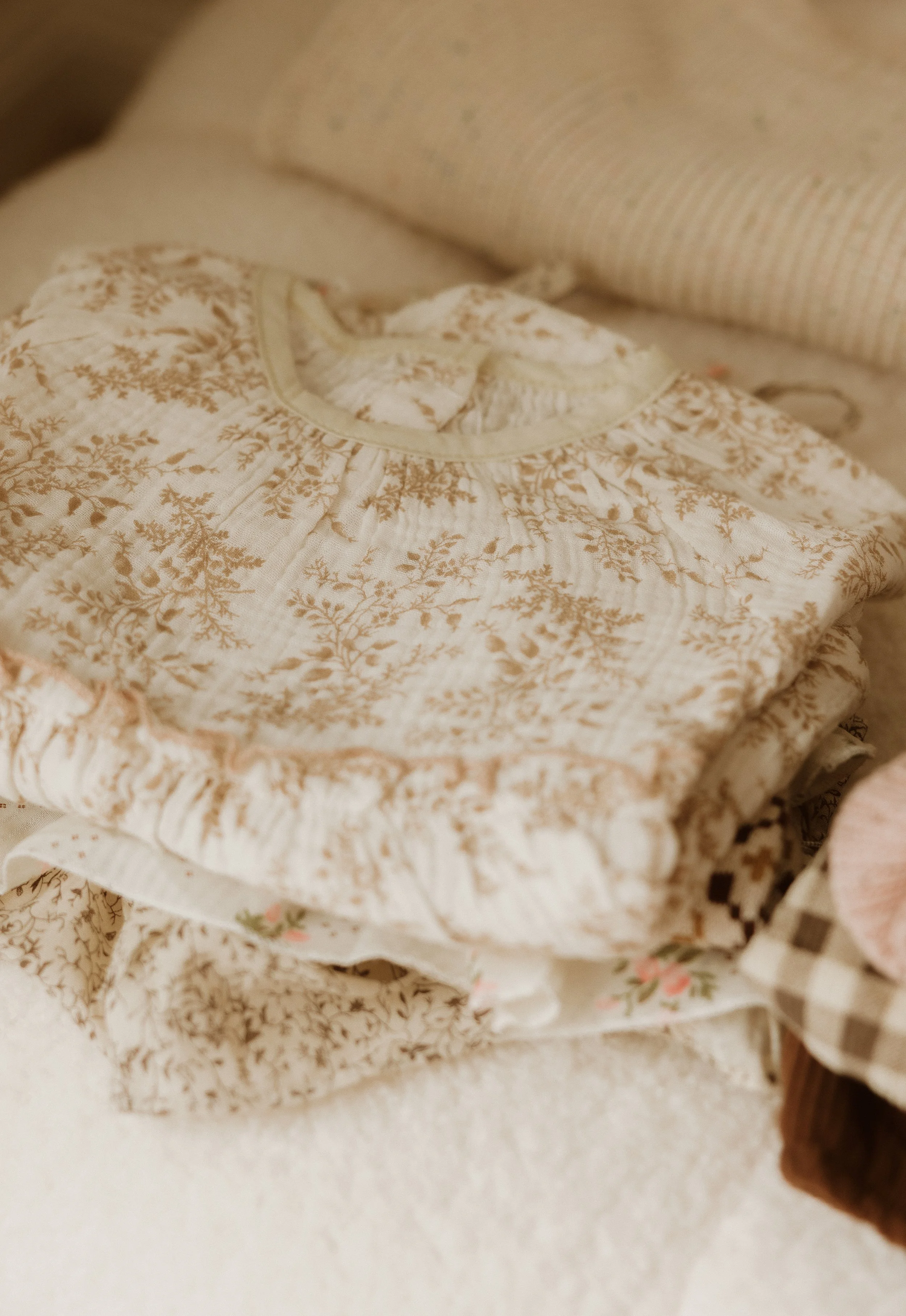 Stacked vintage baby clothes with floral and plaid patterns.