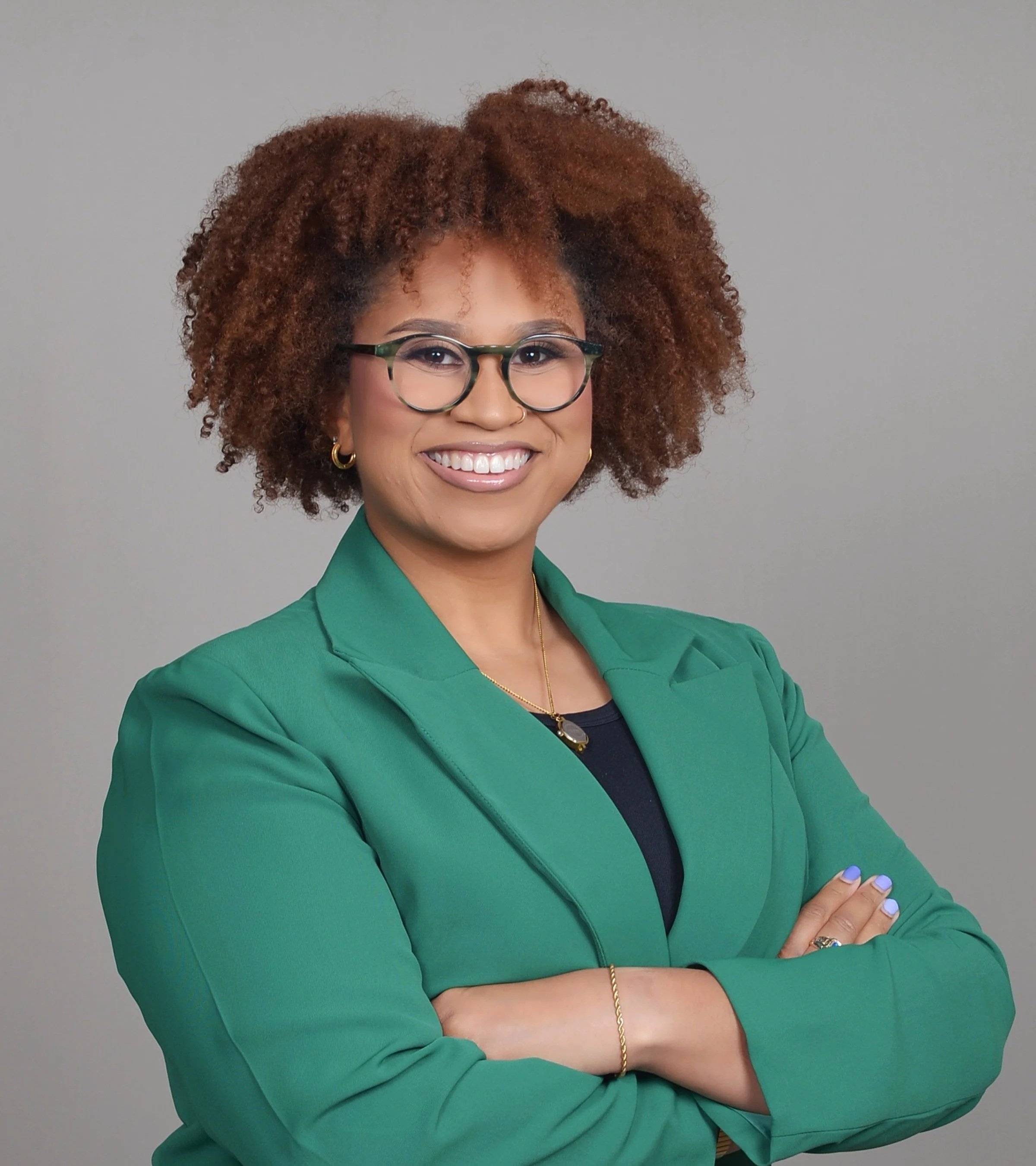 Person in a white turtleneck and light gray blazer smiling outdoors.