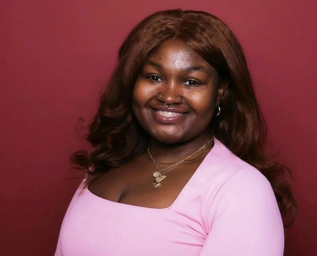Person smiling, wearing a maroon Harvard sweatshirt, with long hair and a nose ring.