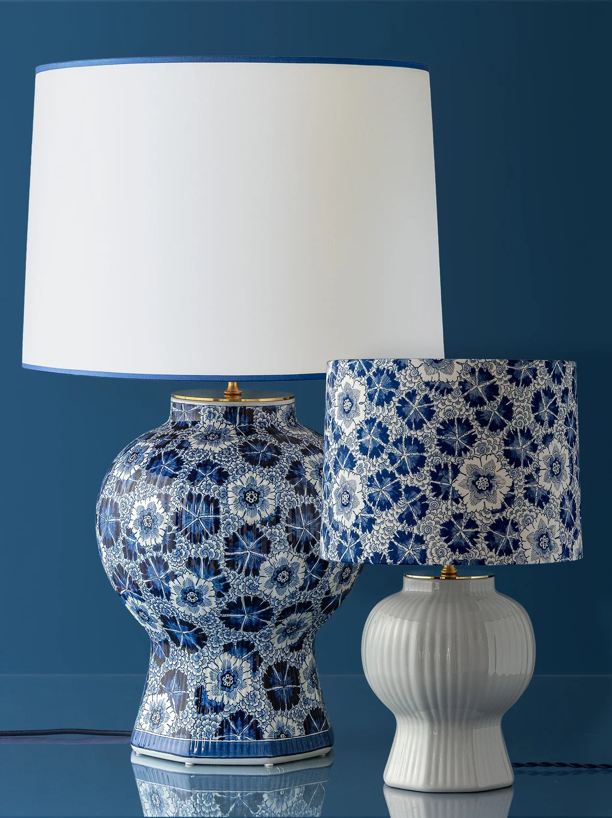 Two decorative table lamps with blue and white floral patterned shades and bases, on a reflective surface against a blue wall.