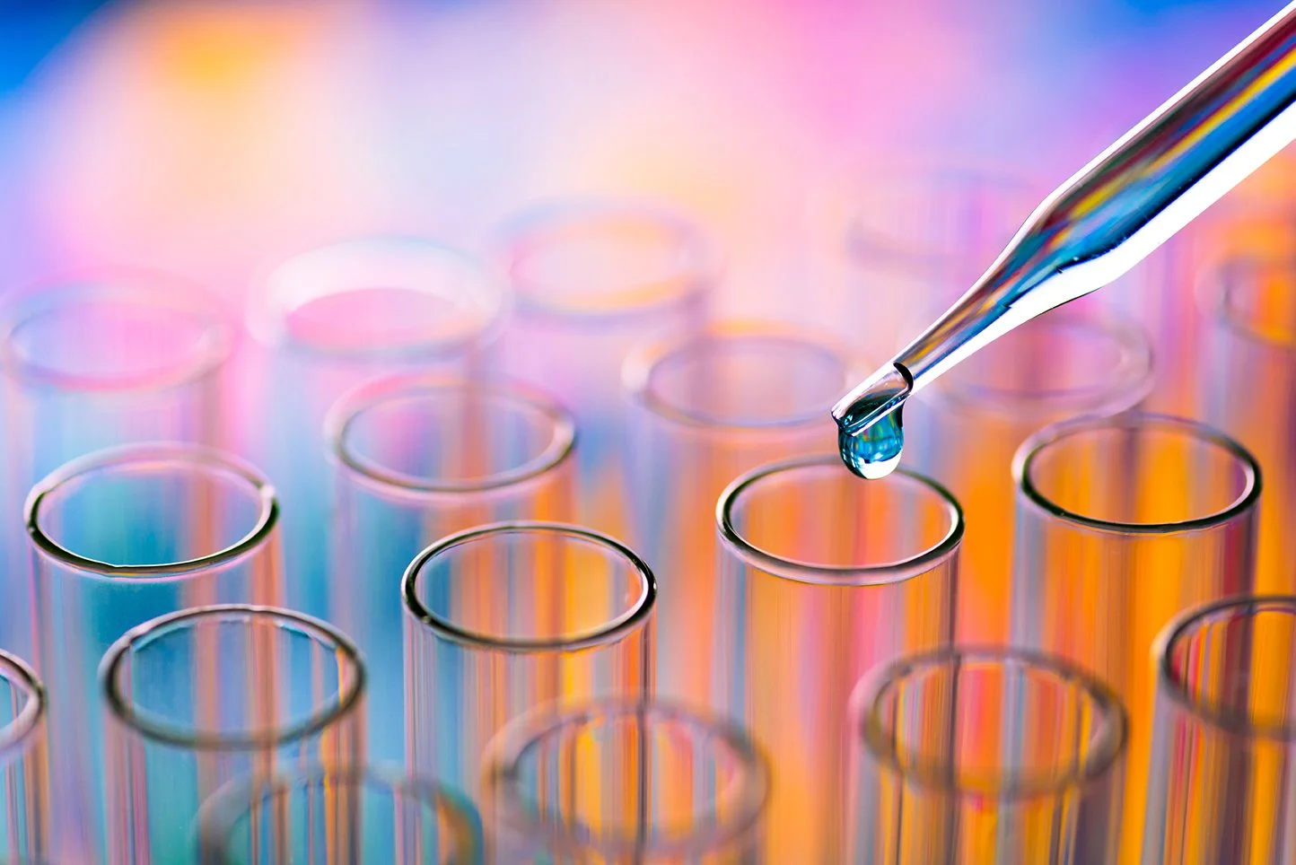 Colourful focussed image of solution dripping from pipette into test tubes