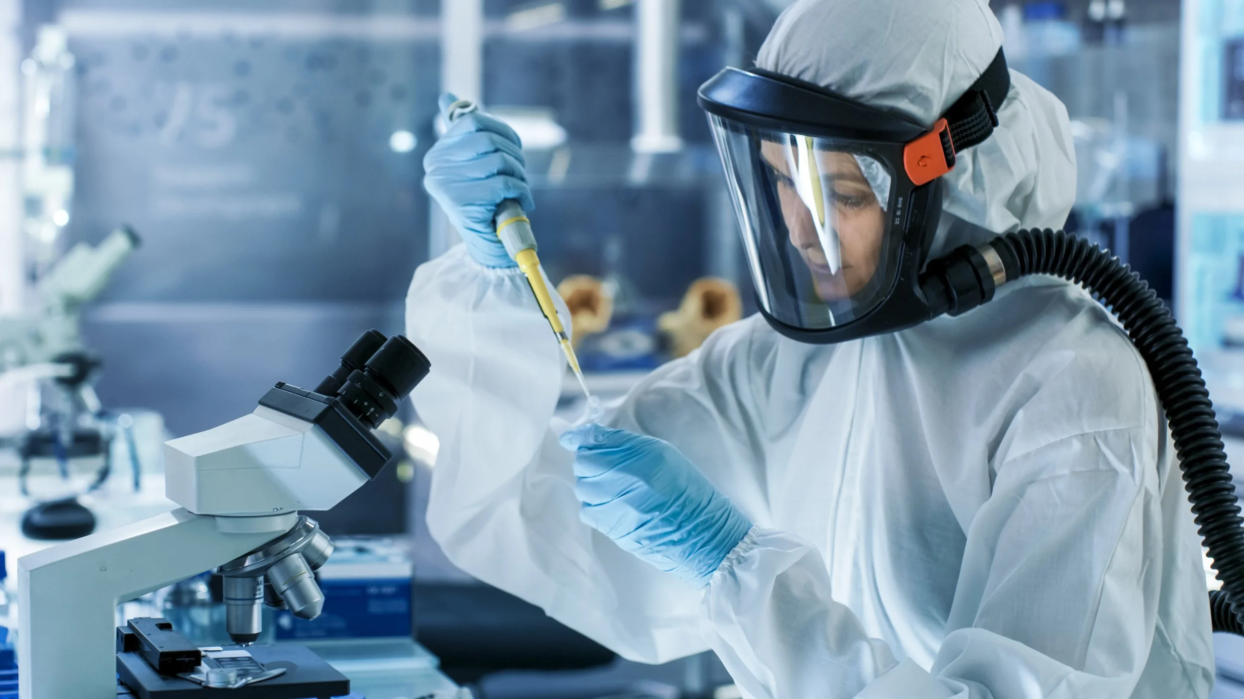 Person wearing protective clothing using specialist equipment in front of microscope in biocontainment