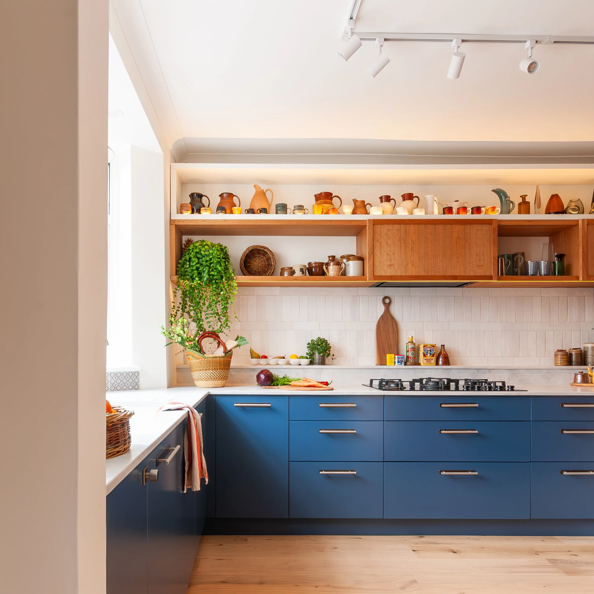 East Dulwich kitchen design with Farrow & Ball Stiffkey Blue cabinetry, cherry wood display cabinets, white textured splashback tiles and pottery collection