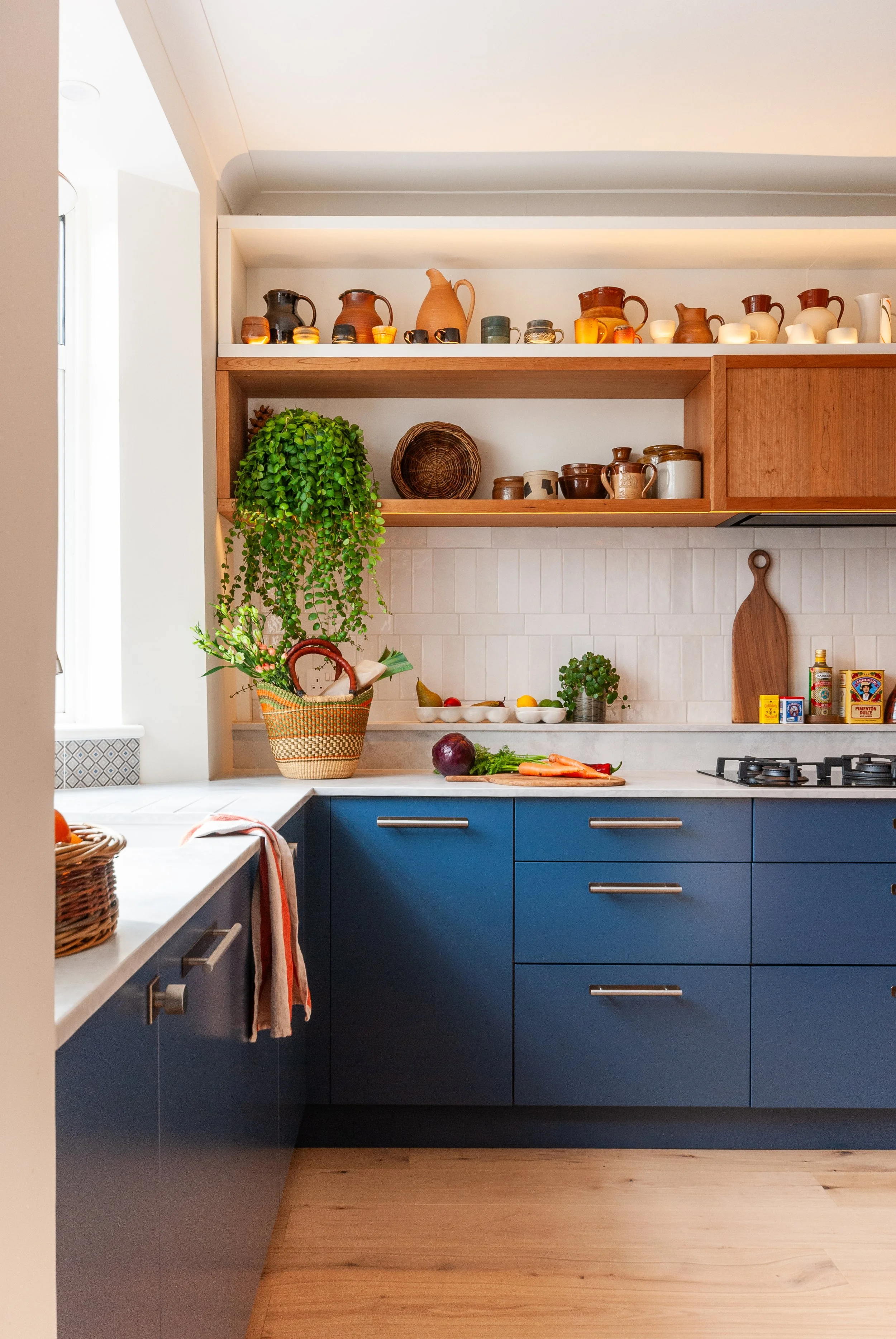 Blue and cherry wood kitchen in East Dulwich with open display shelving, everyday storage, plants and warm timber details.
