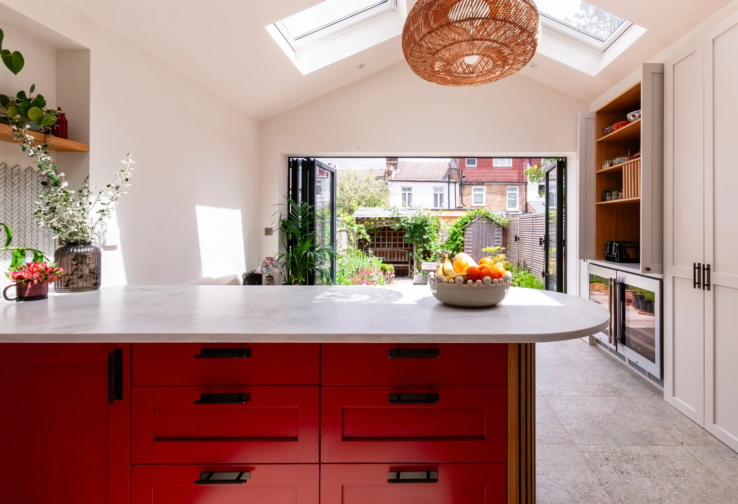 Red kitchen extension in Forest Hill designed for indoor-outdoor living, with a curved peninsula, vaulted ceiling, rooflights and garden views
