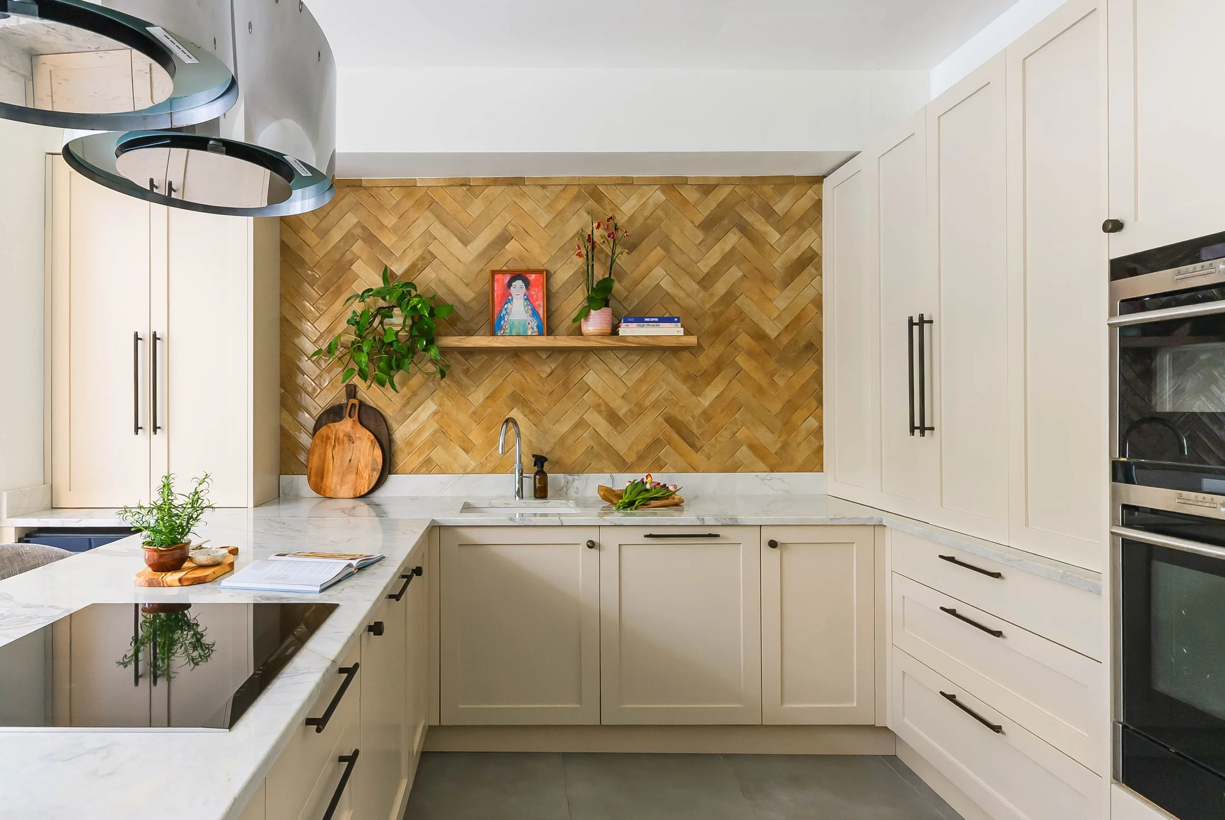 Forest Hill bespoke kitchen with cream shaker cabinetry, natural quartzite worktops, antique brass handles, integrated ovens and full-height herringbone tiled splashback.